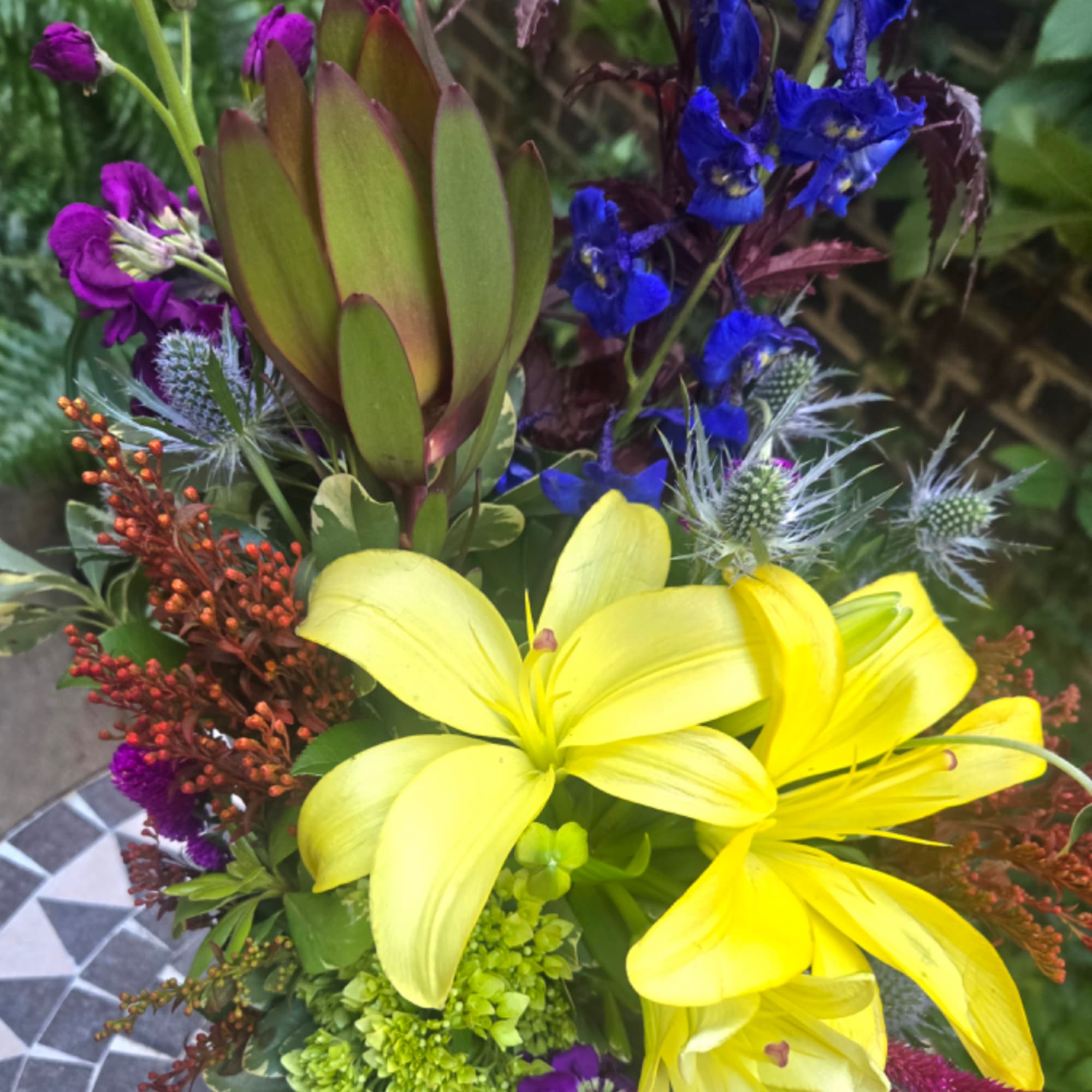 Bouquet with yellow lilies, blue flowers, and a large green protea