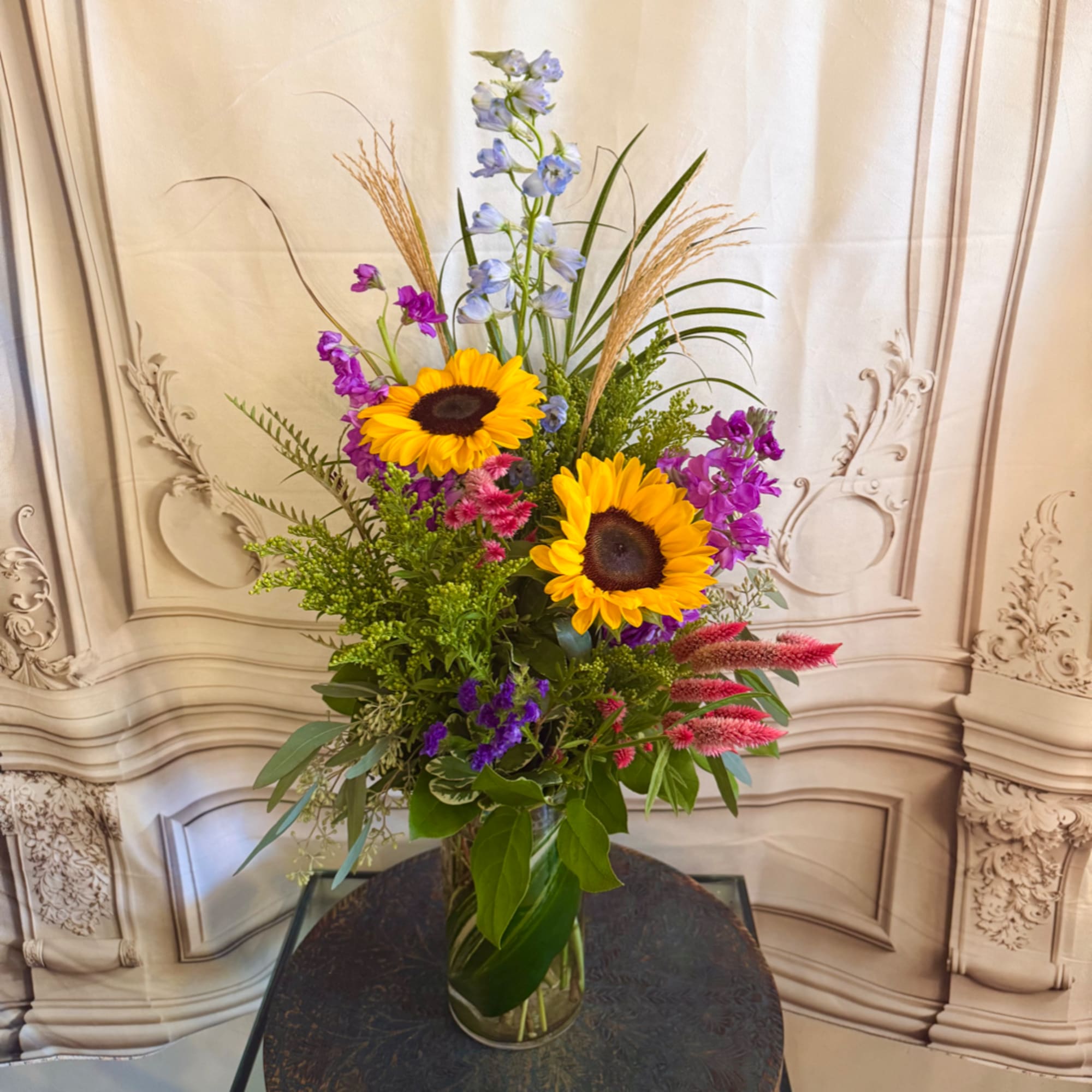 Tall mixed bouquet with sunflowers, purple blooms, and a glass vase