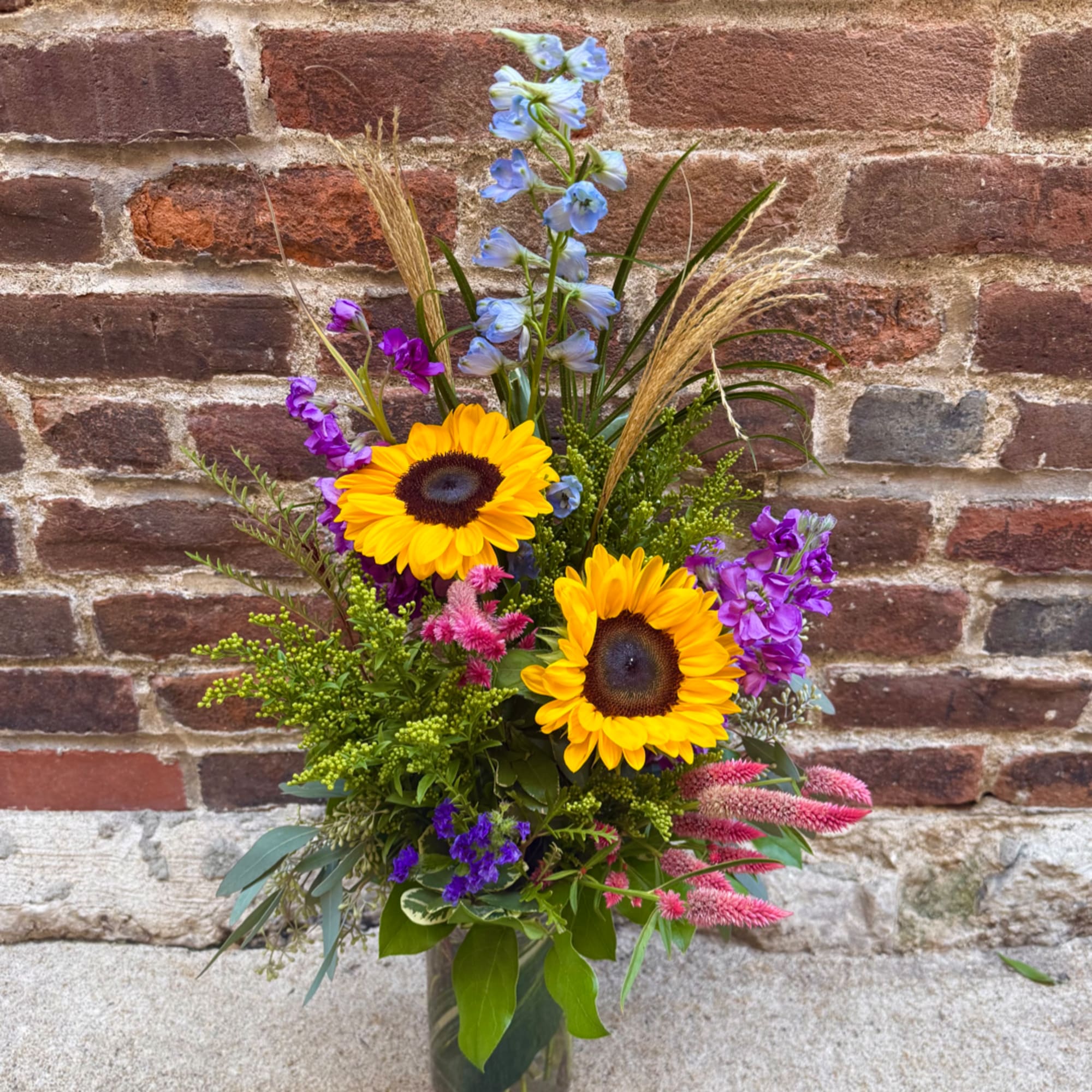 Mixed bouquet with sunflowers, purple blooms, and blue flowers in a glass vase