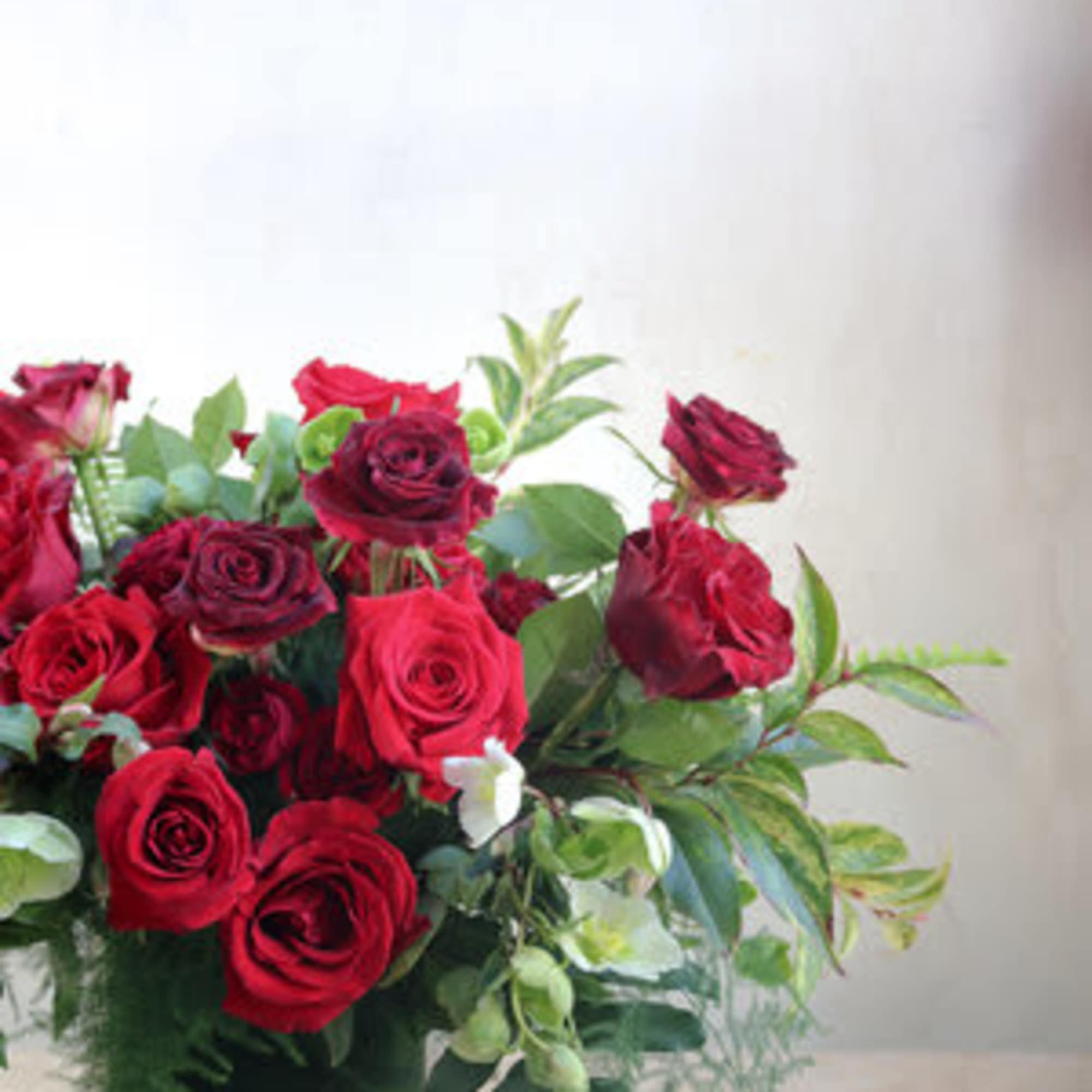 Red roses arranged in a clear square vase with greenery