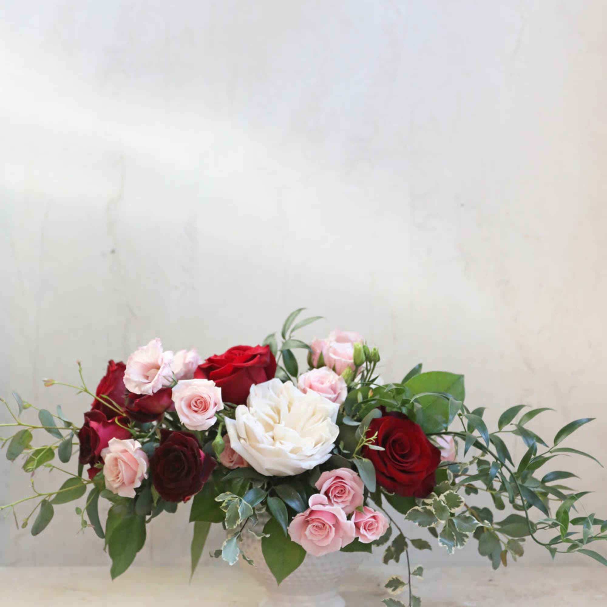 Low arrangement of red, pink, and white roses in a white vase