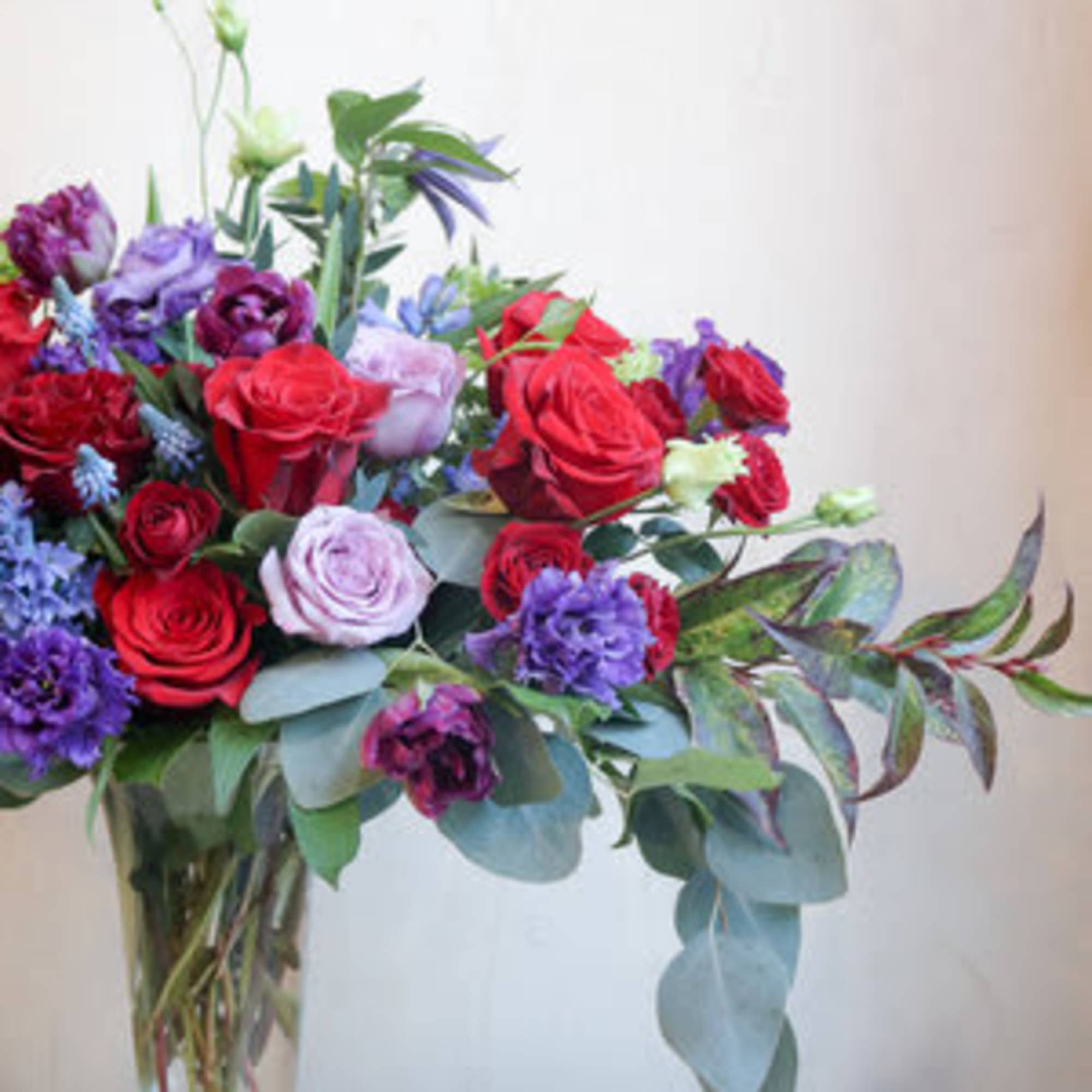 Mixed bouquet of red, purple, and lavender flowers in a clear glass vase
