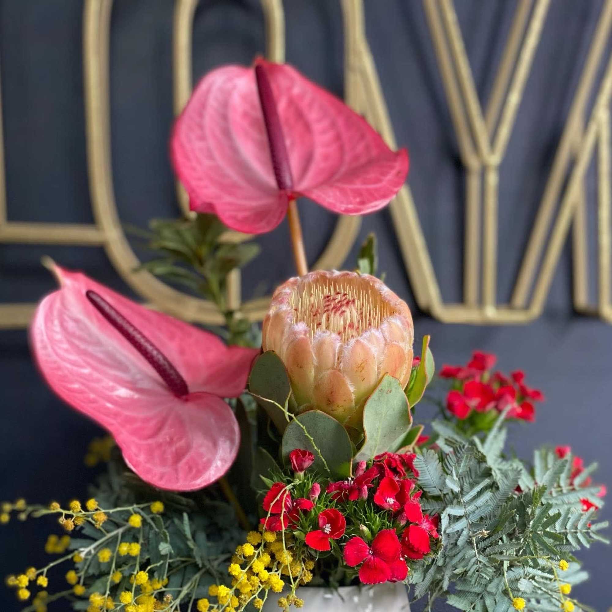 Pink anthuriums with red flowers and yellow filler in a white container