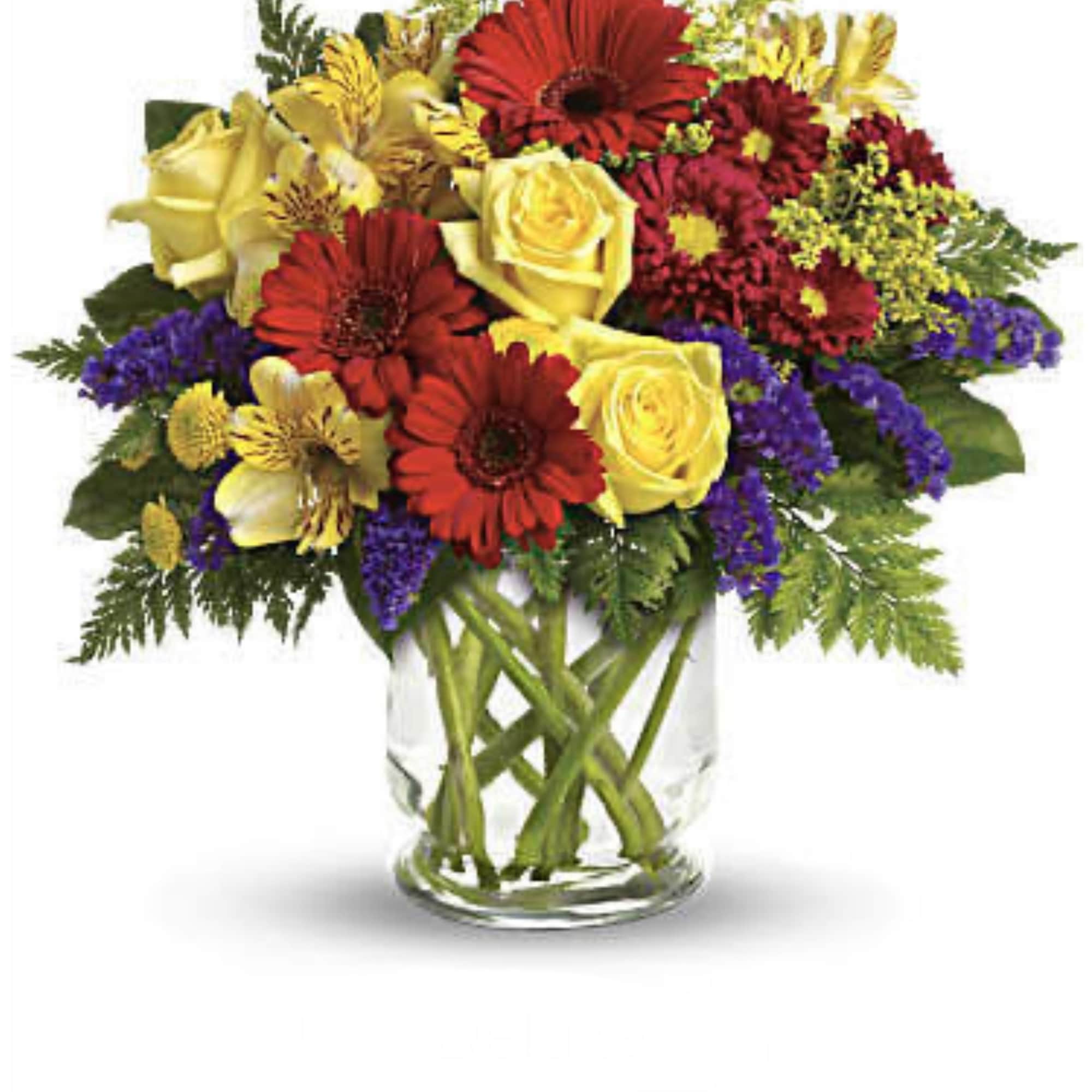 Mixed bouquet of red gerberas, yellow roses, and purple filler in a glass vase