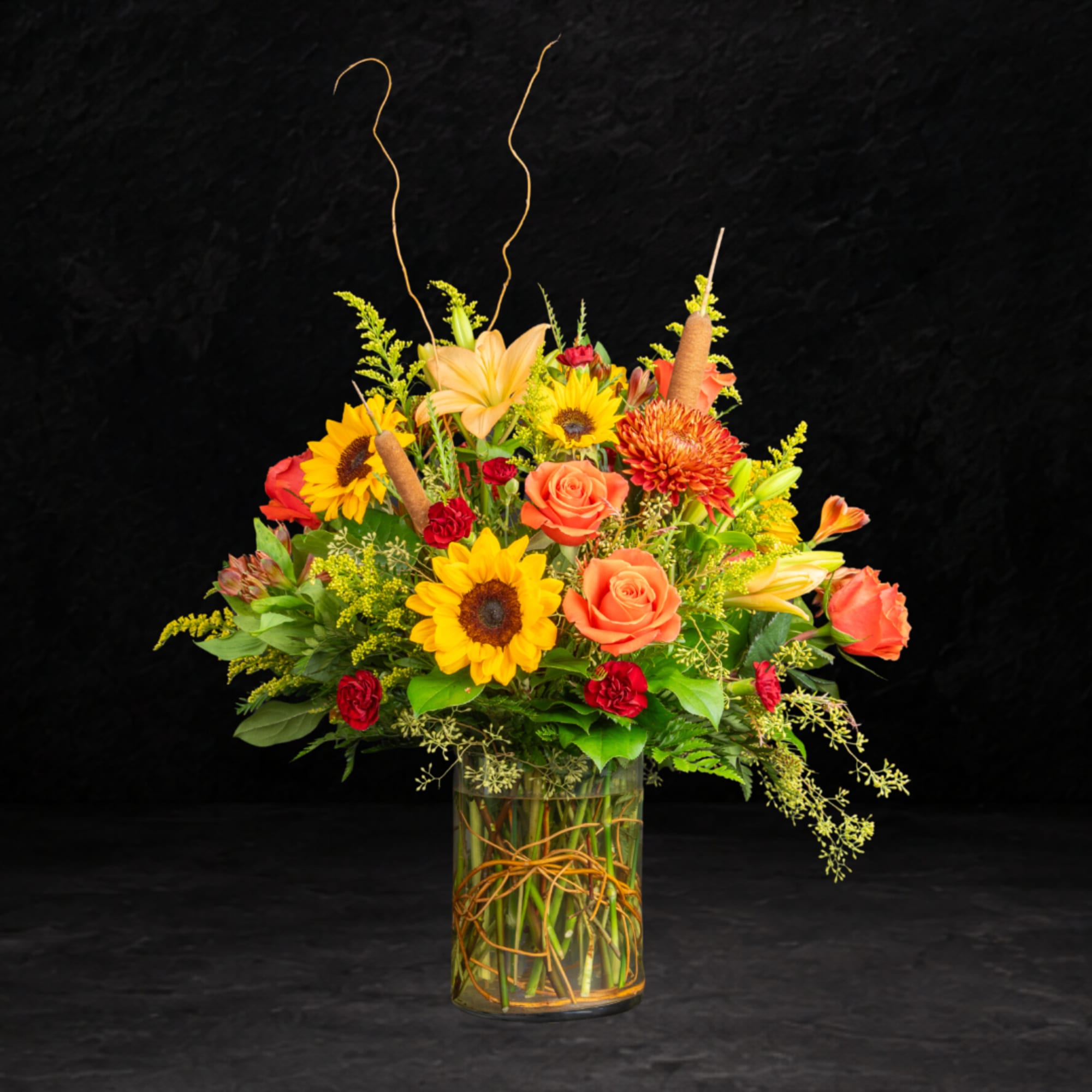 Mixed bouquet in a glass vase with sunflowers, roses, and lilies