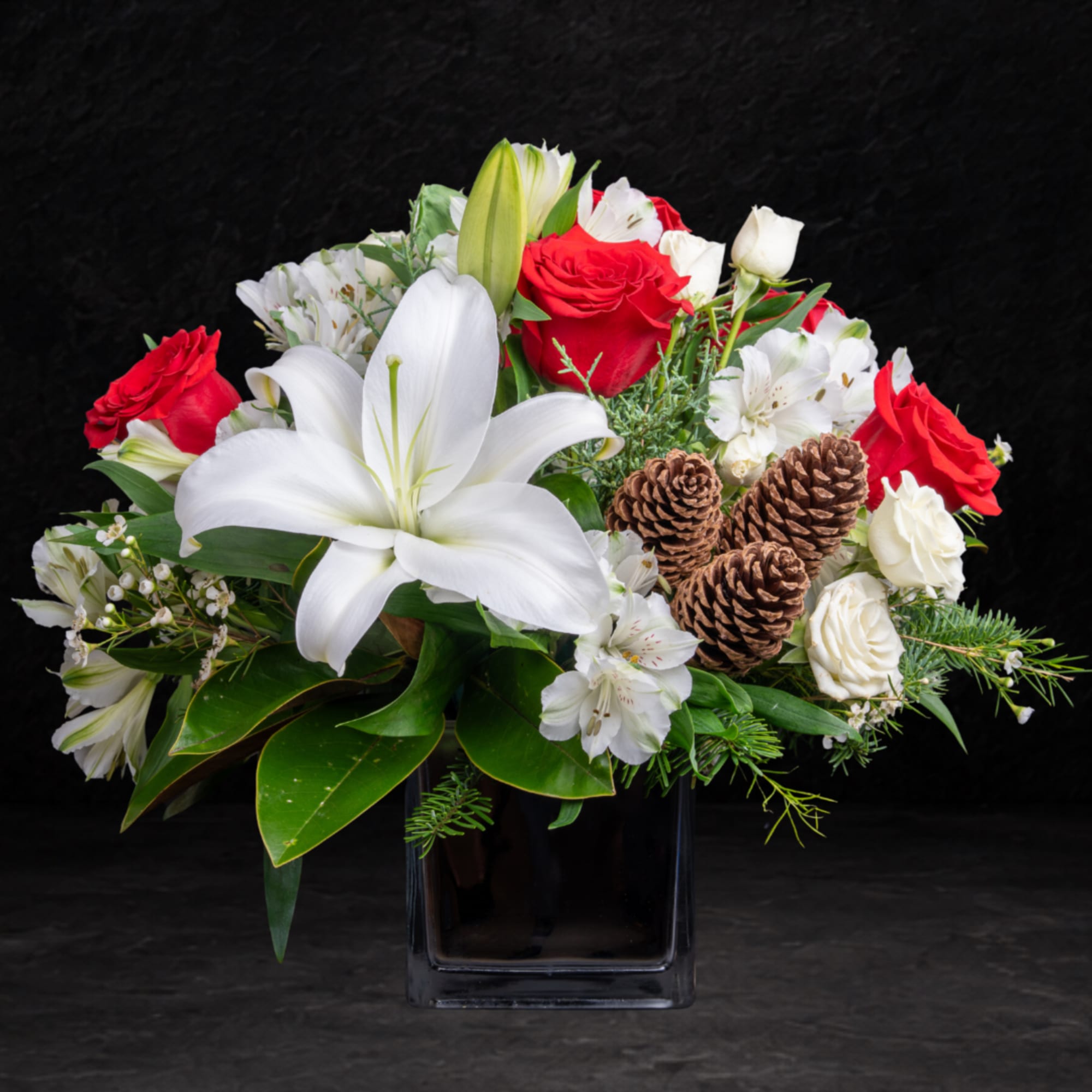 White lilies and red roses in a black vase with pinecones