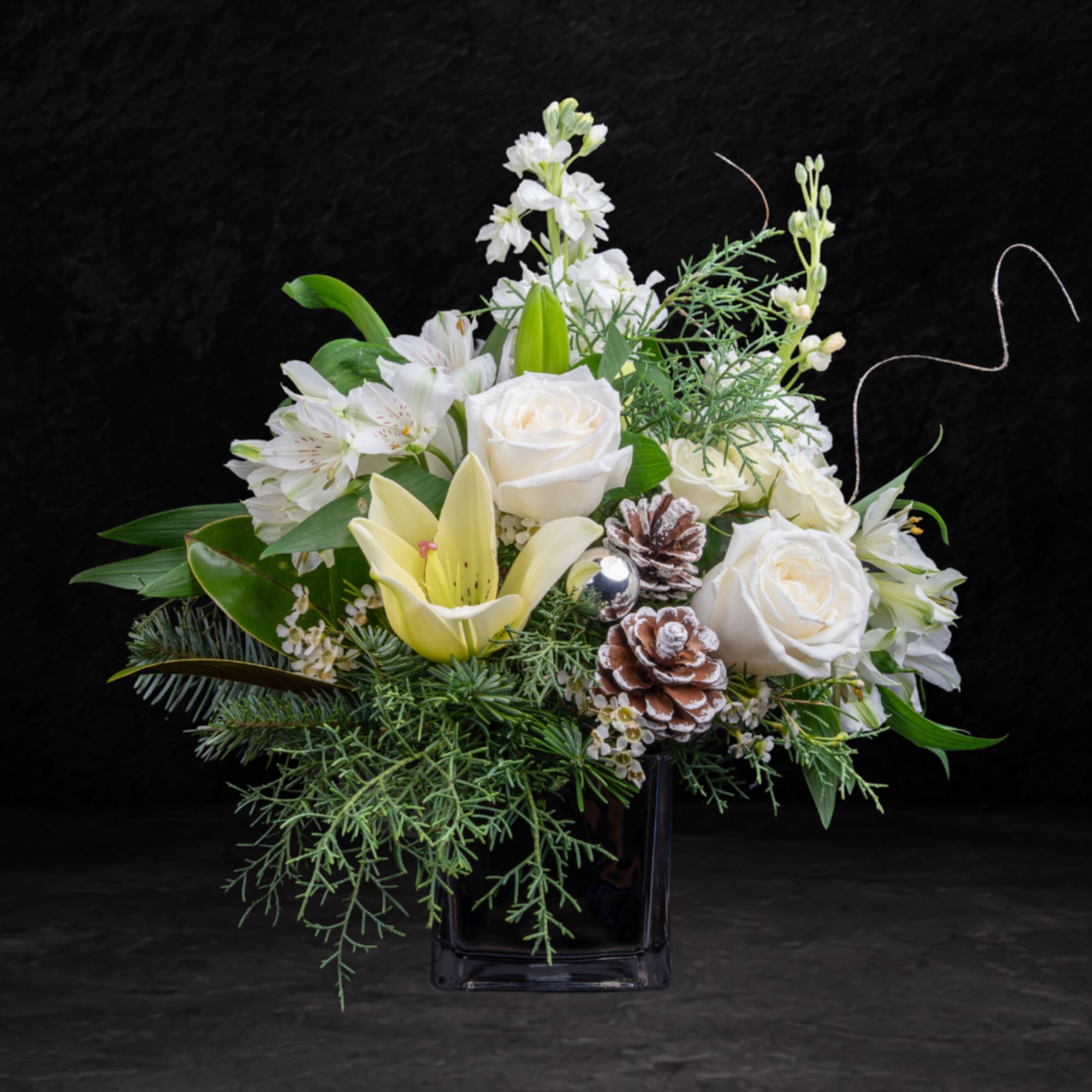 White roses and lilies in a black vase with pinecones