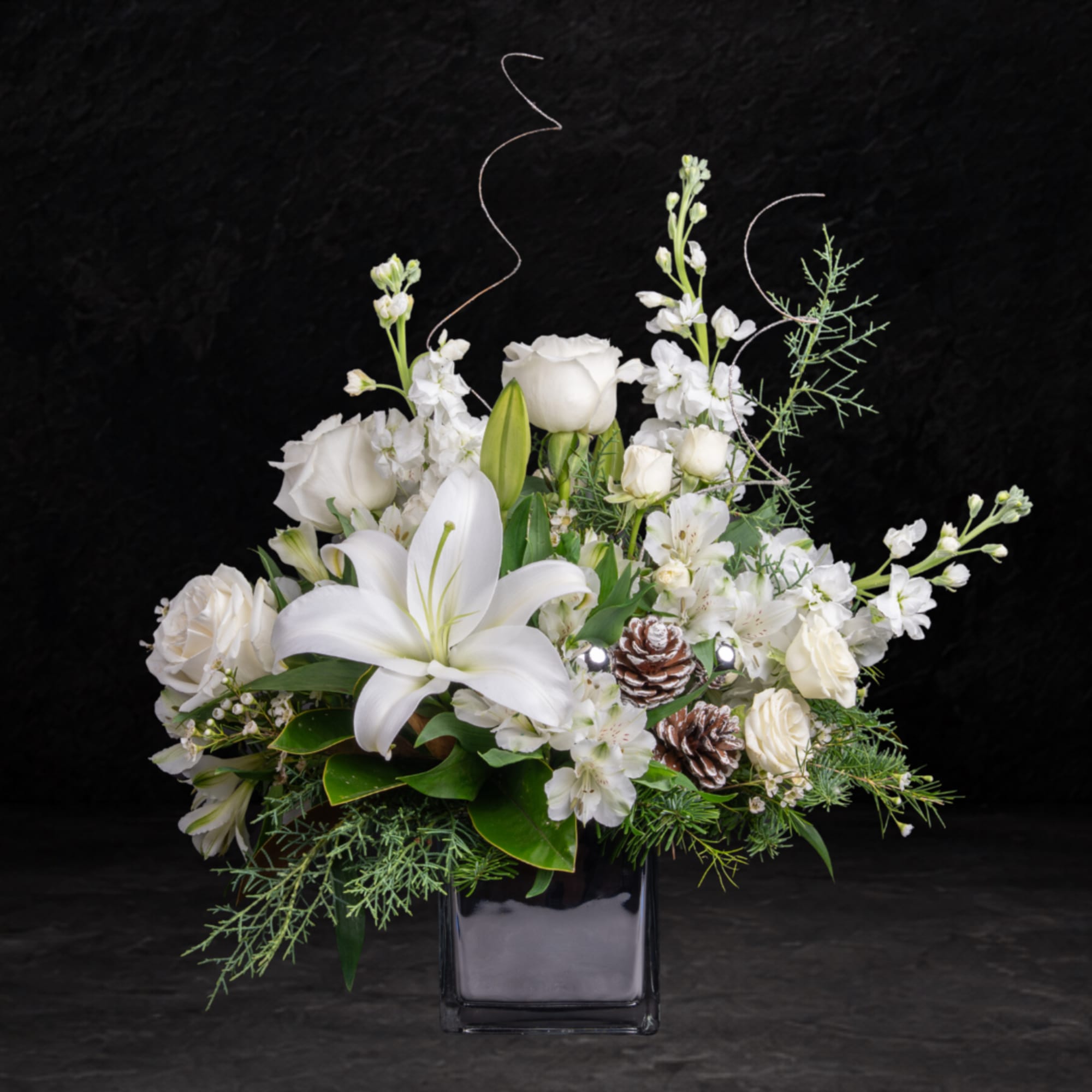 White lilies and roses in a black glass vase with pinecones