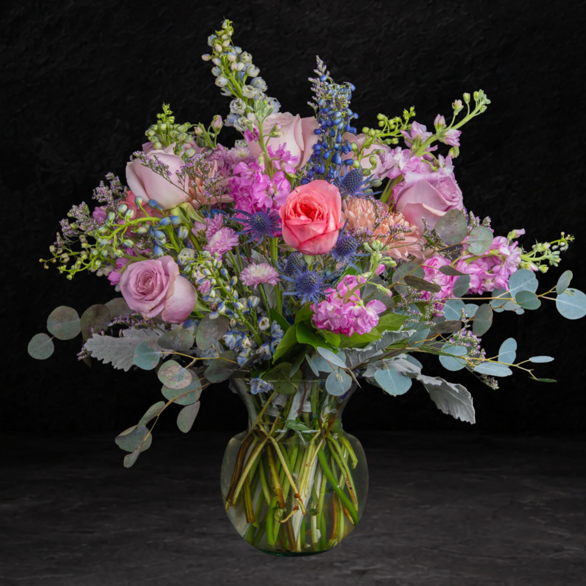 Mixed bouquet of pink, lavender, and blue flowers in a clear glass vase
