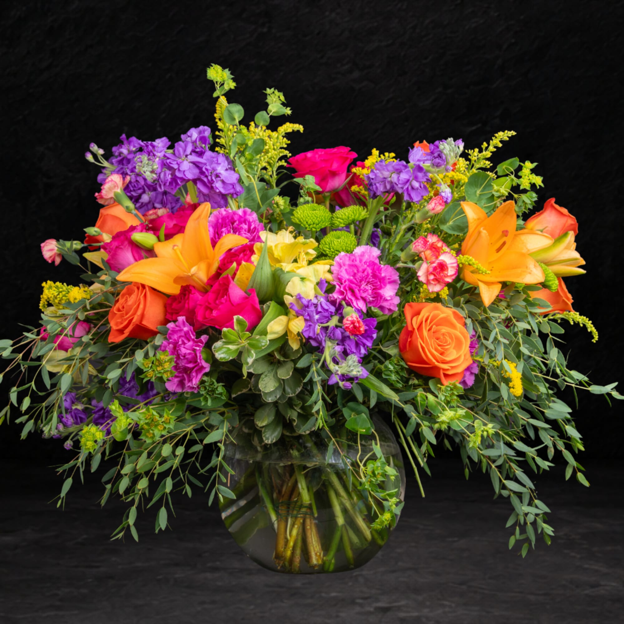 Colorful mixed bouquet in a clear glass vase with orange lilies and roses