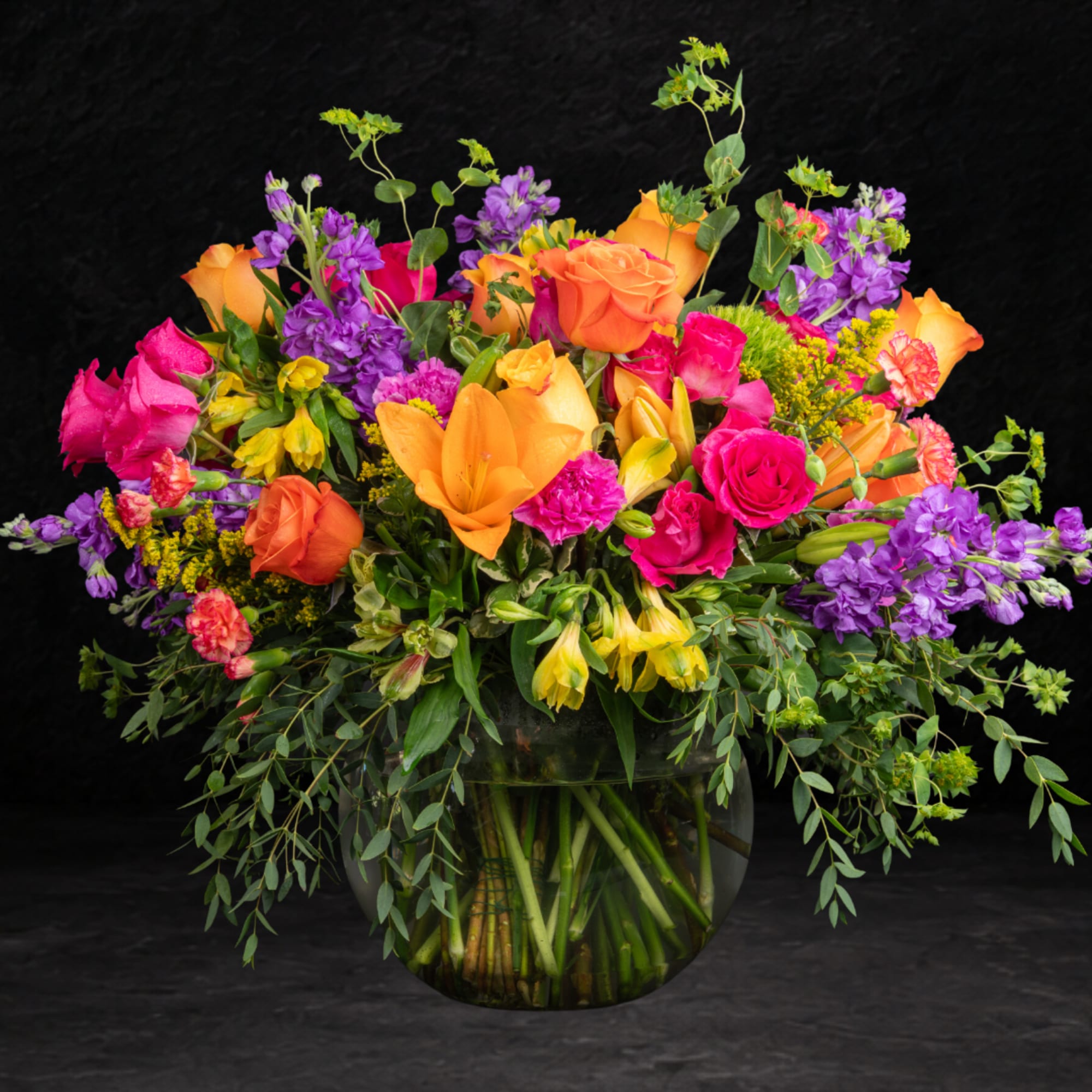 Colorful mixed bouquet in a clear glass vase with roses and lilies