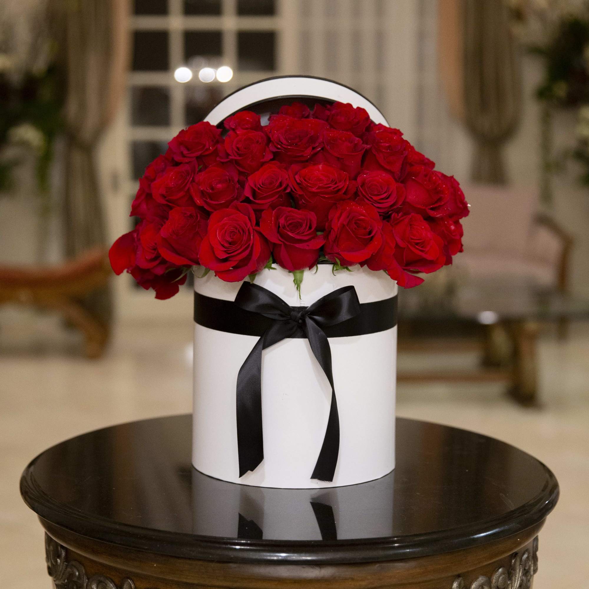 Red roses arranged in a white hatbox with a black ribbon