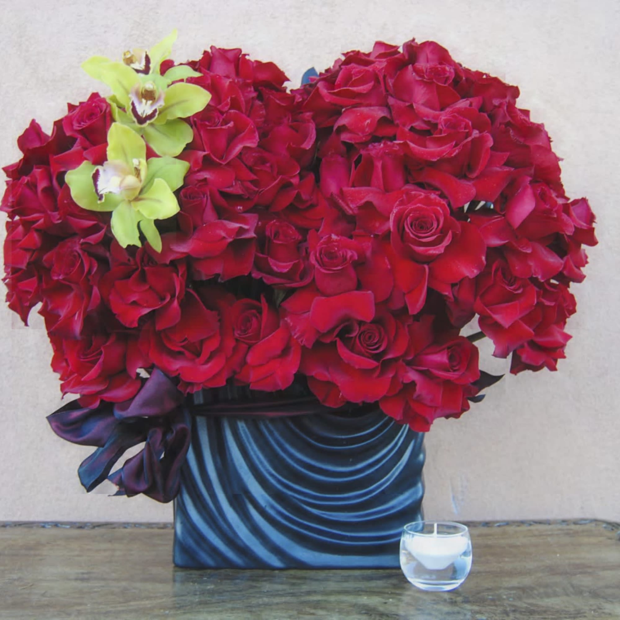 Red rose arrangement in a blue vase with two green orchids