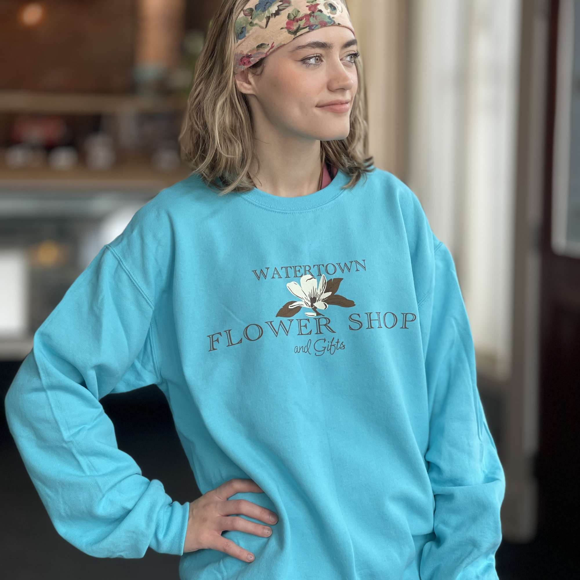 Woman wearing a turquoise flower shop sweatshirt and floral headband