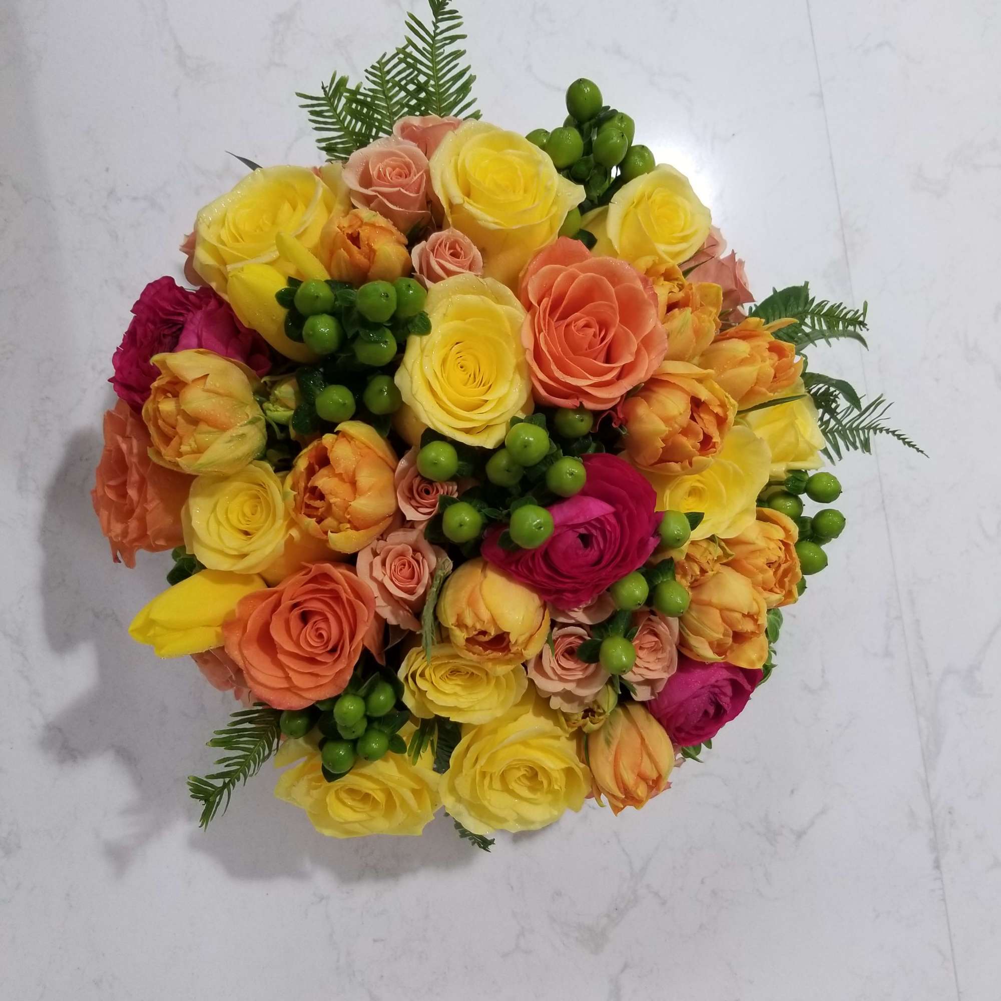 Round bouquet of yellow, peach, and pink roses with green berries