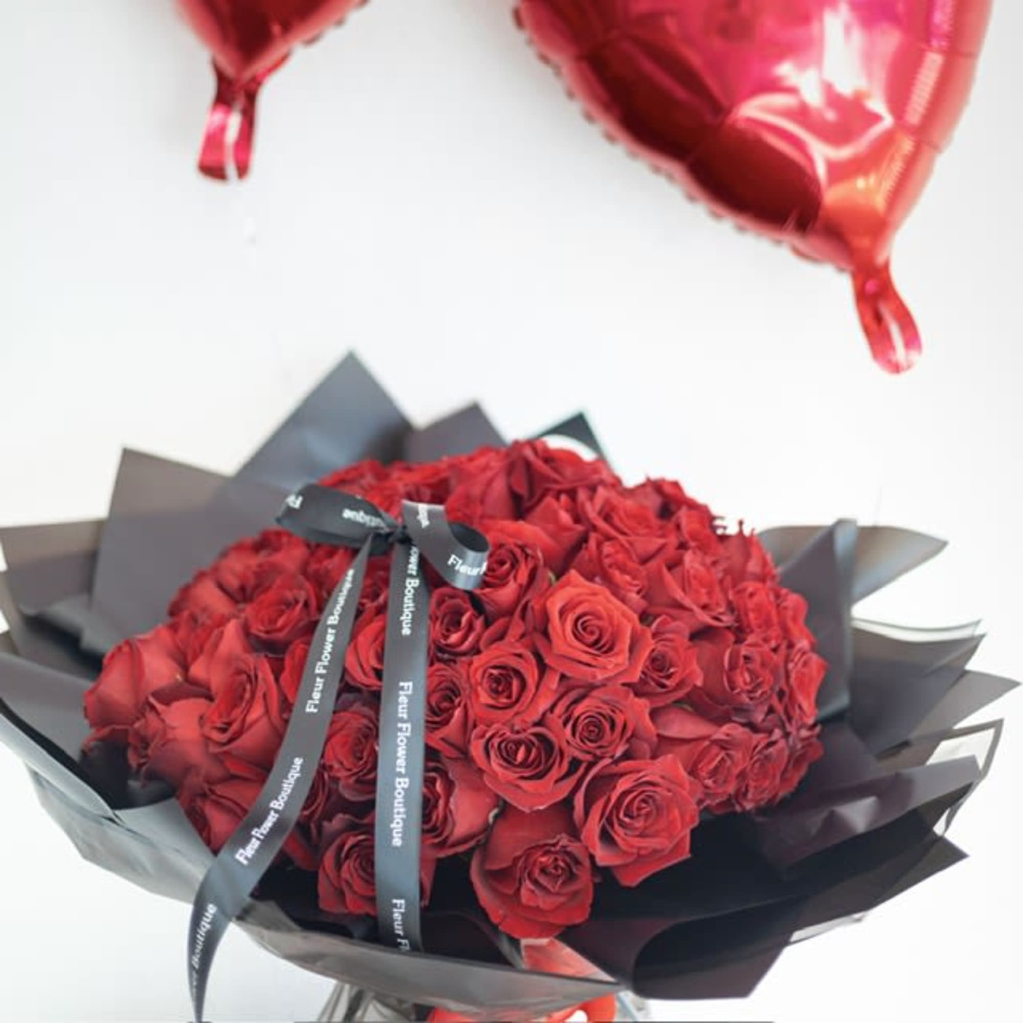 Bouquet of red roses wrapped in black paper with red balloons above