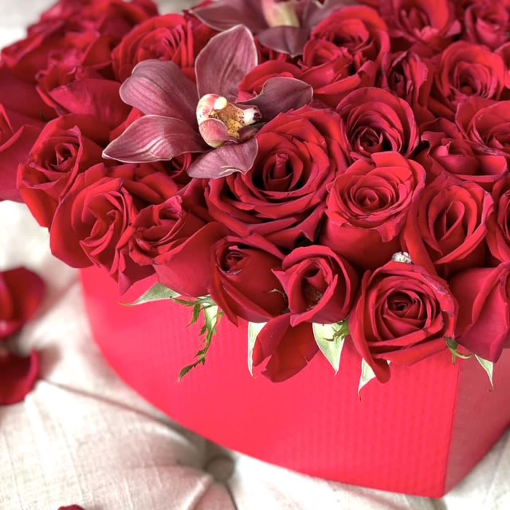 Red roses arranged in a pink box with a purple orchid accent