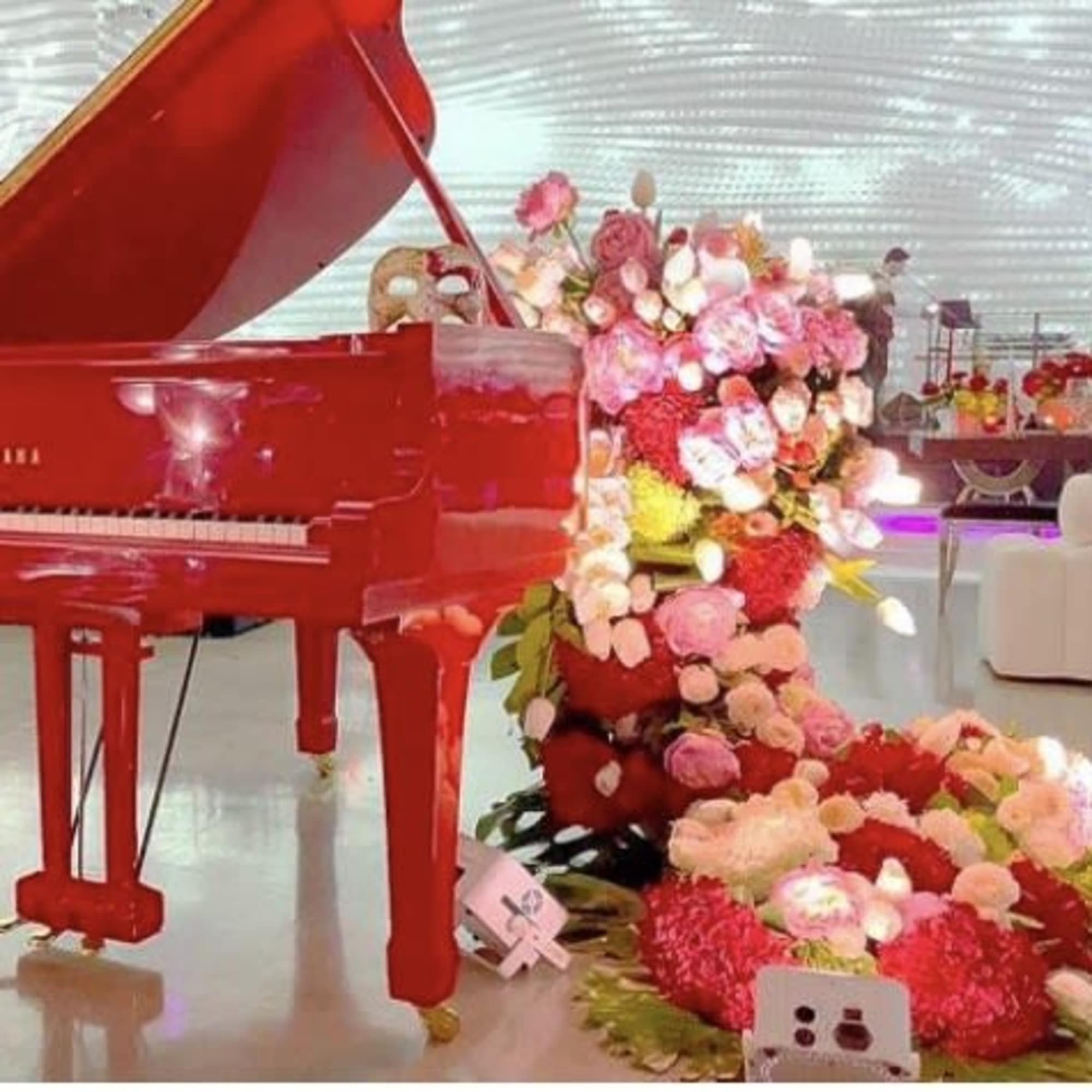 Red grand piano beside a large pink and red floral display