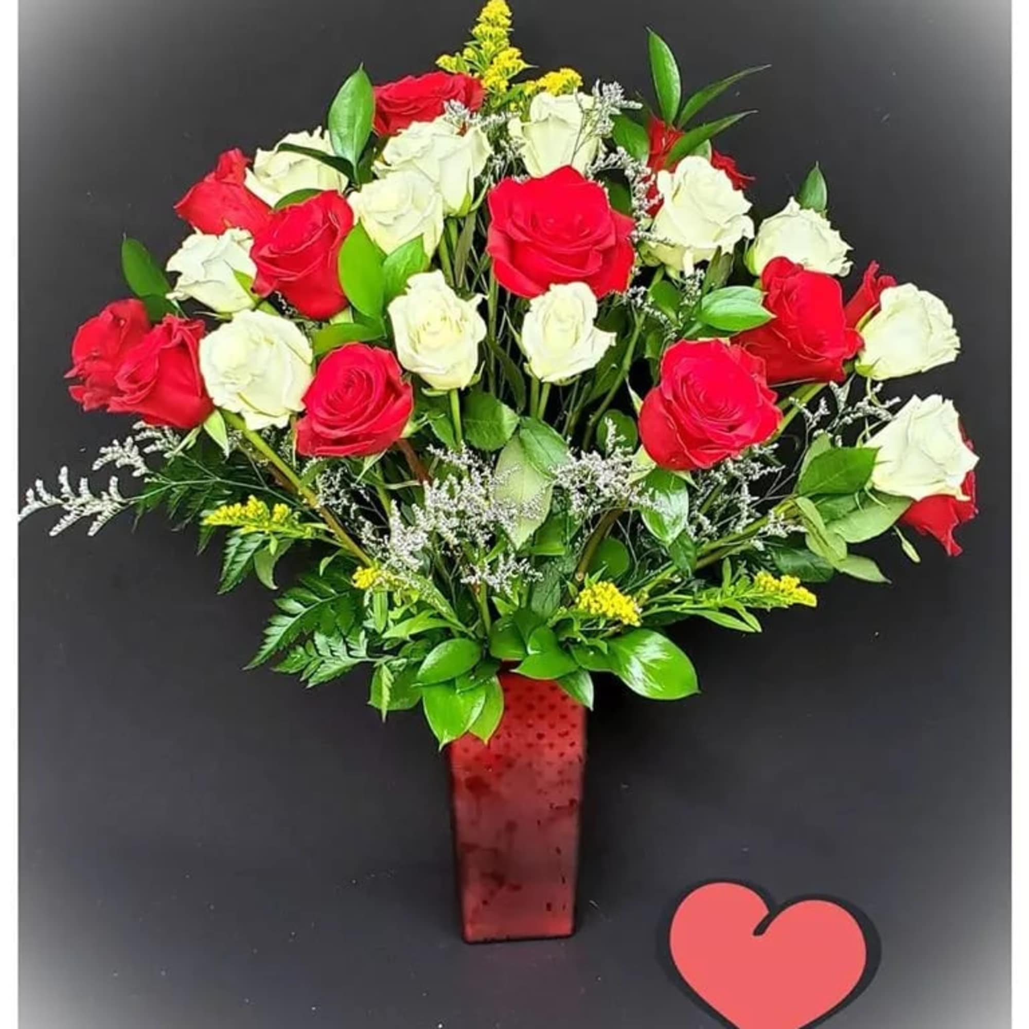 Red and white roses arranged in a red vase with a heart decoration
