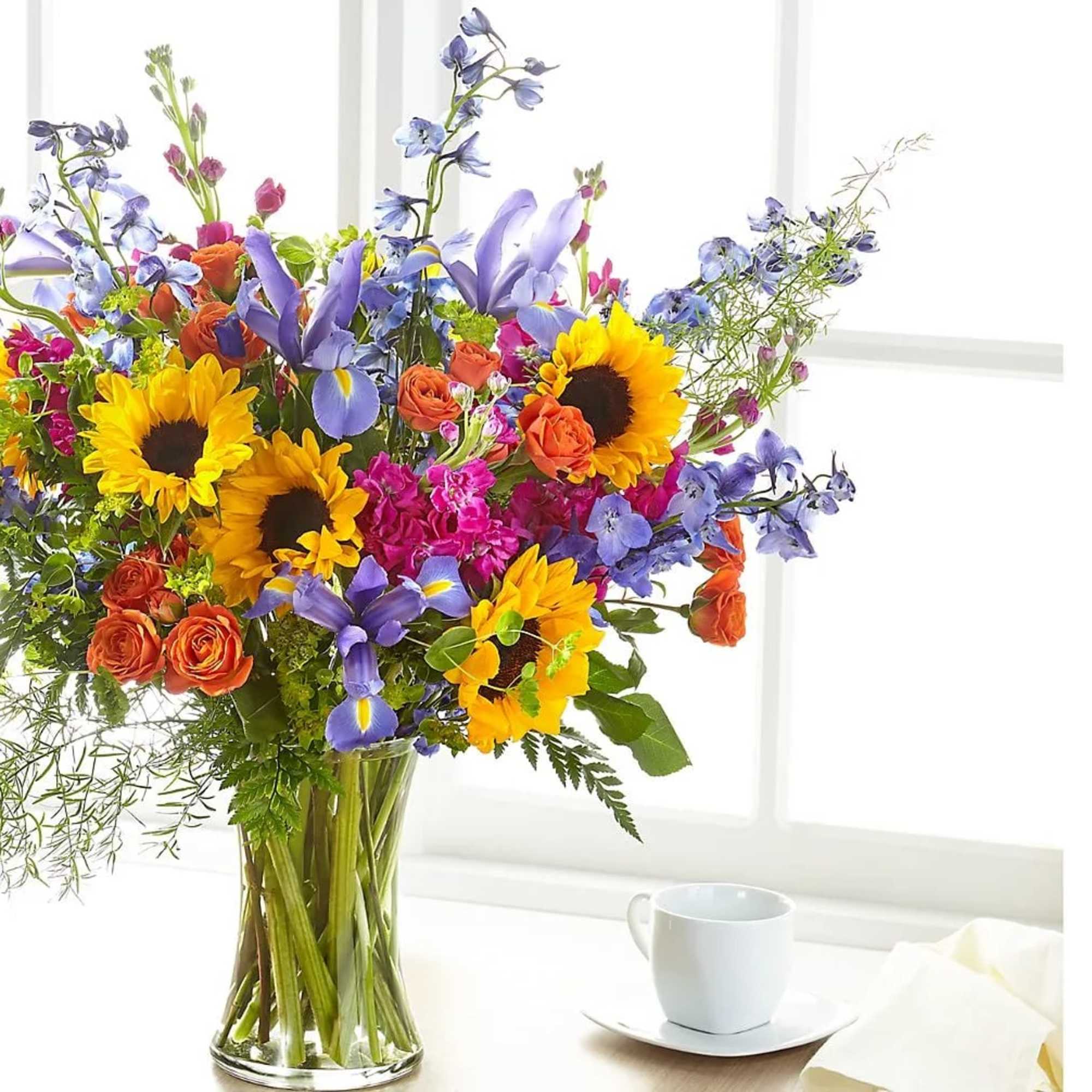 Colorful bouquet of sunflowers, roses, and purple flowers in a glass vase
