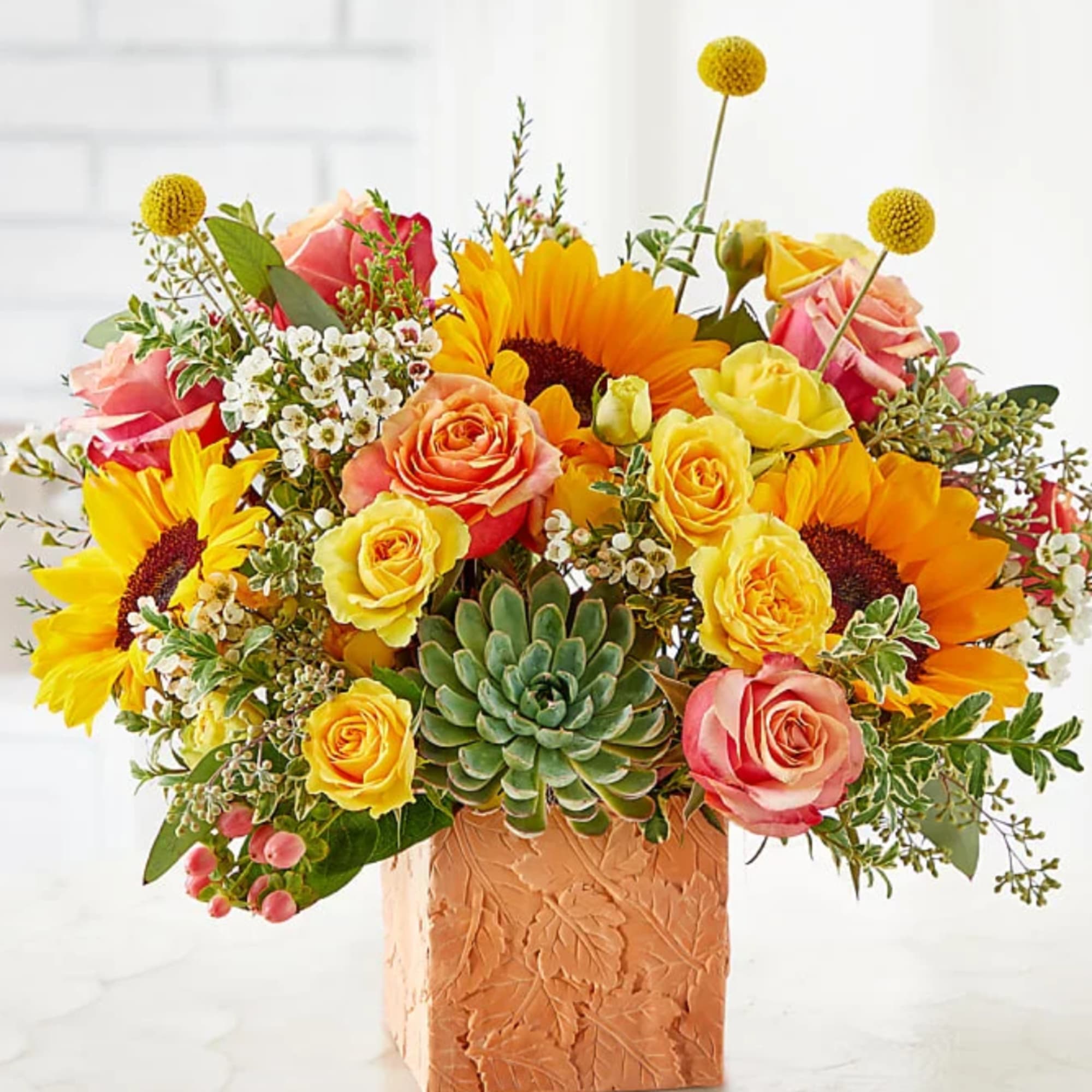 Sunflower and rose arrangement in a textured square vase with a succulent center