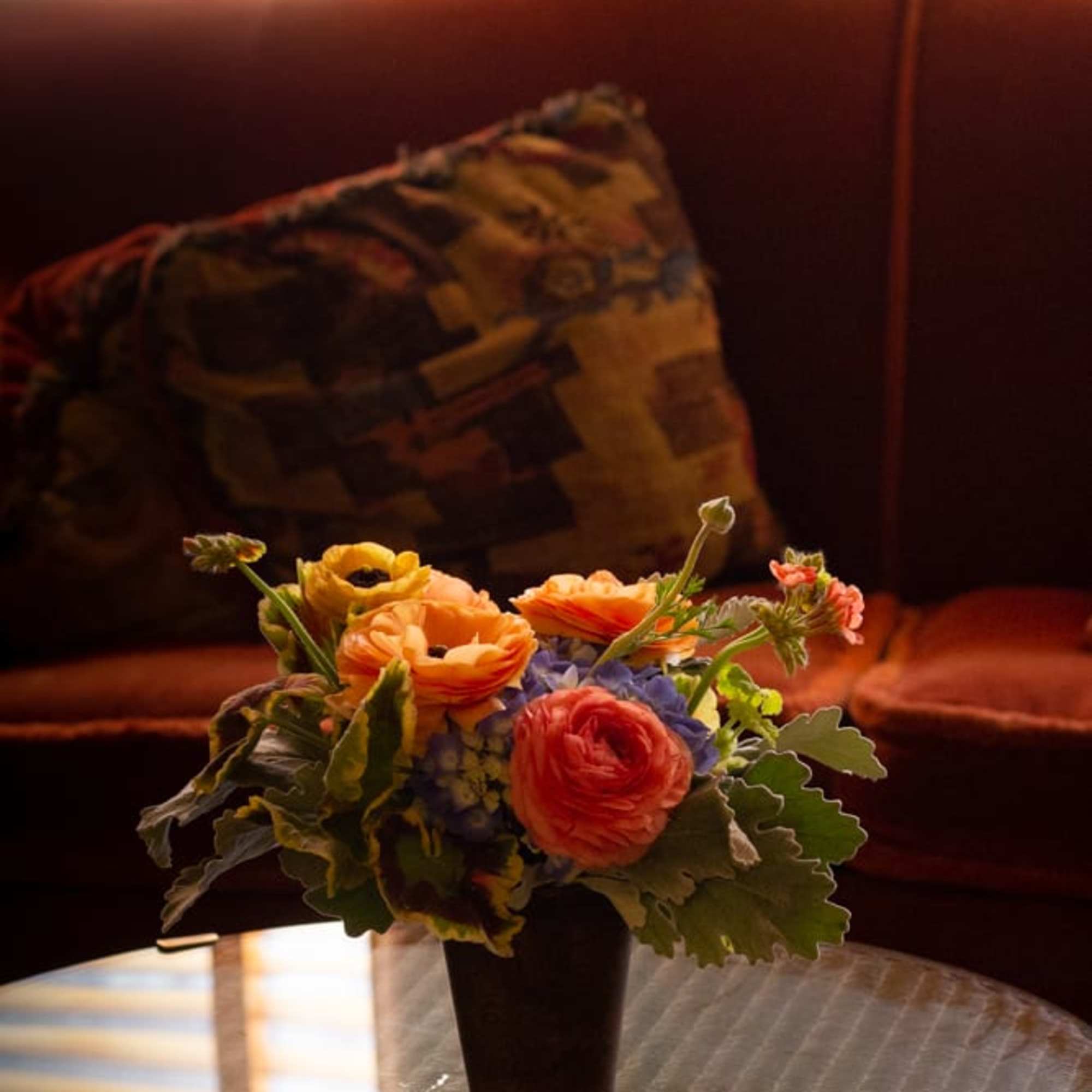 Small mixed flower arrangement in a dark vase on a glass table