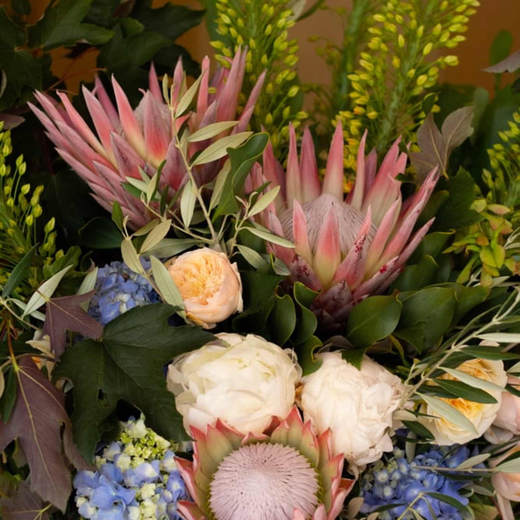 Mixed bouquet with pink protea, blue hydrangeas, and white blooms