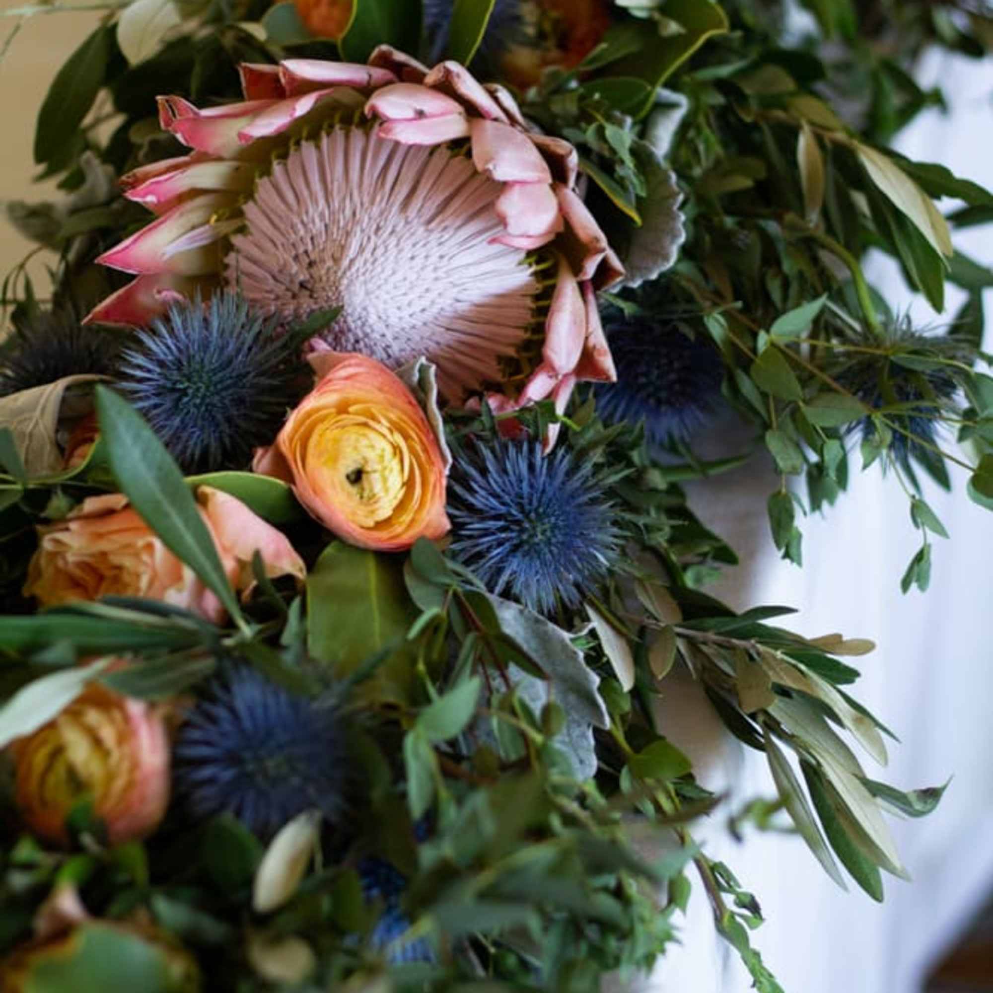 Bouquet with pink protea, orange ranunculus, and blue thistle