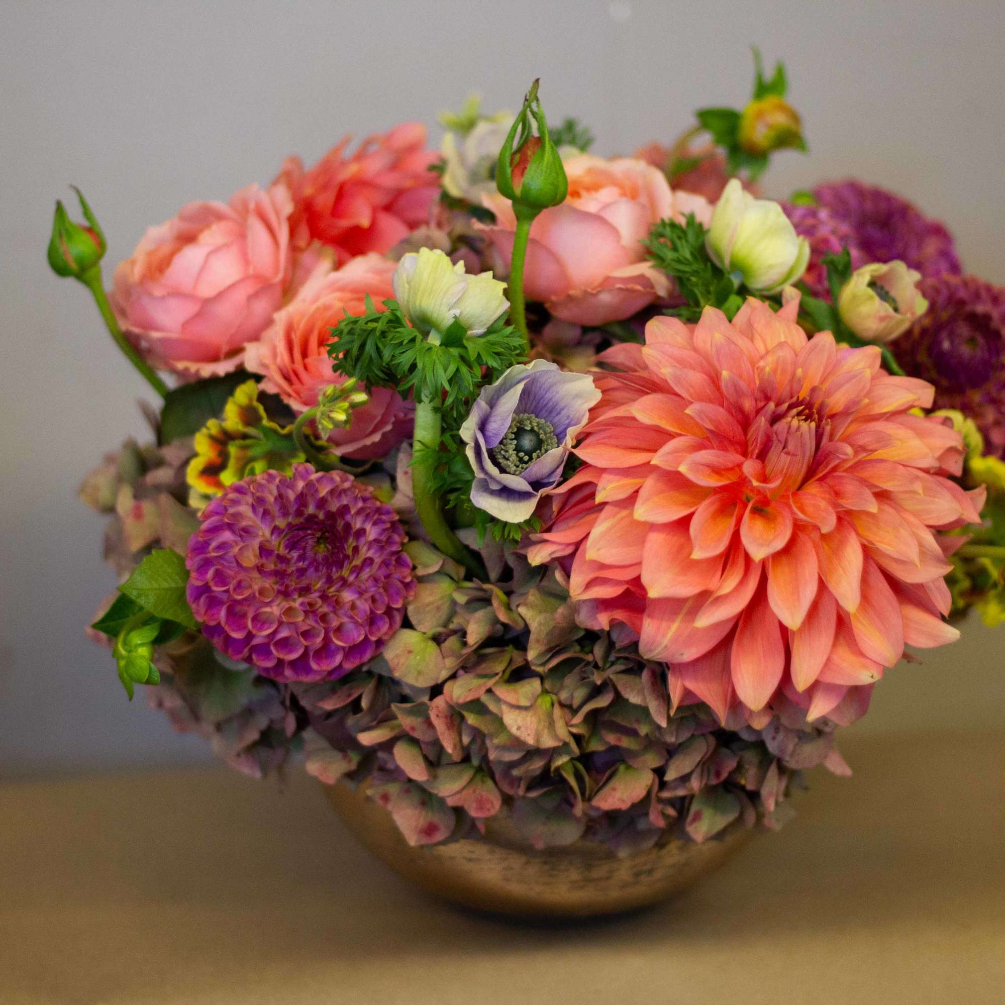 Mixed bouquet of pink, peach, and purple flowers in a low bowl vase