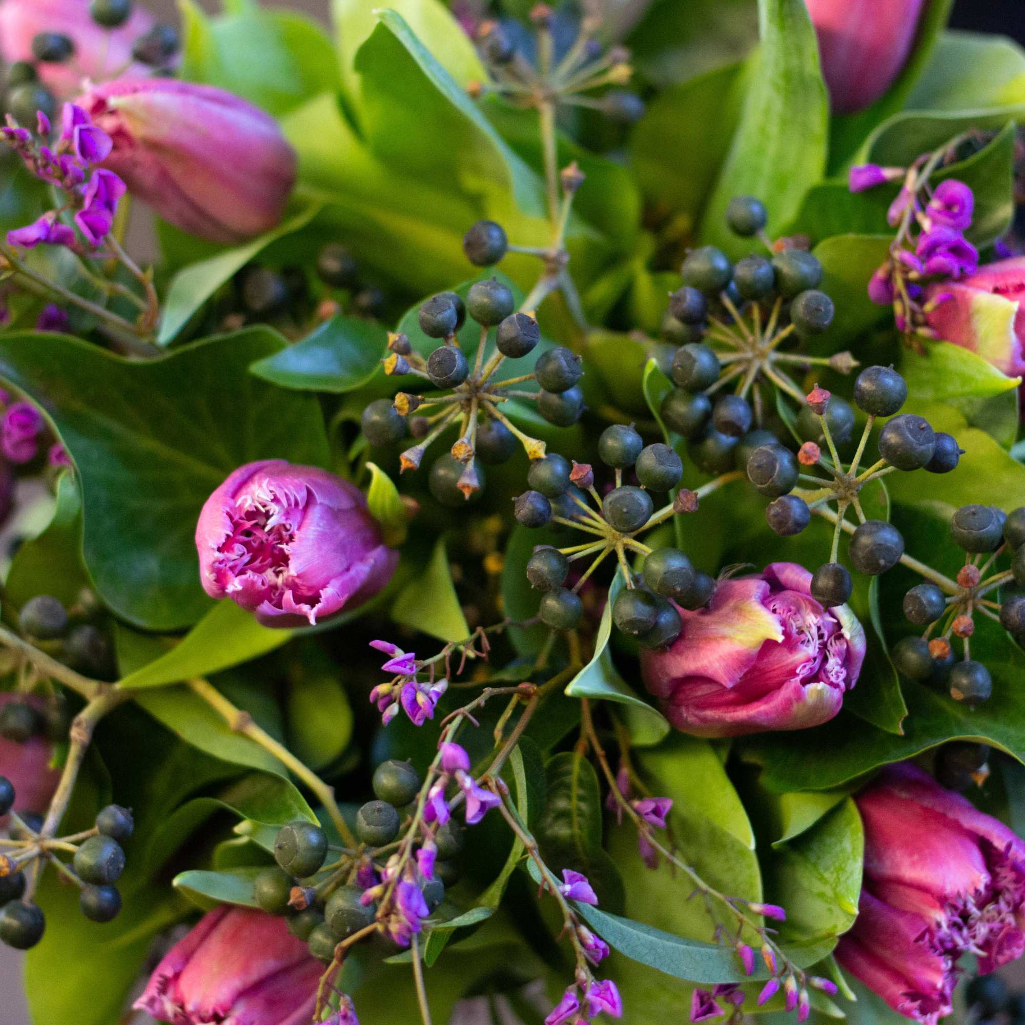 Pink tulips with purple accents and dark berry clusters in a leafy bouquet