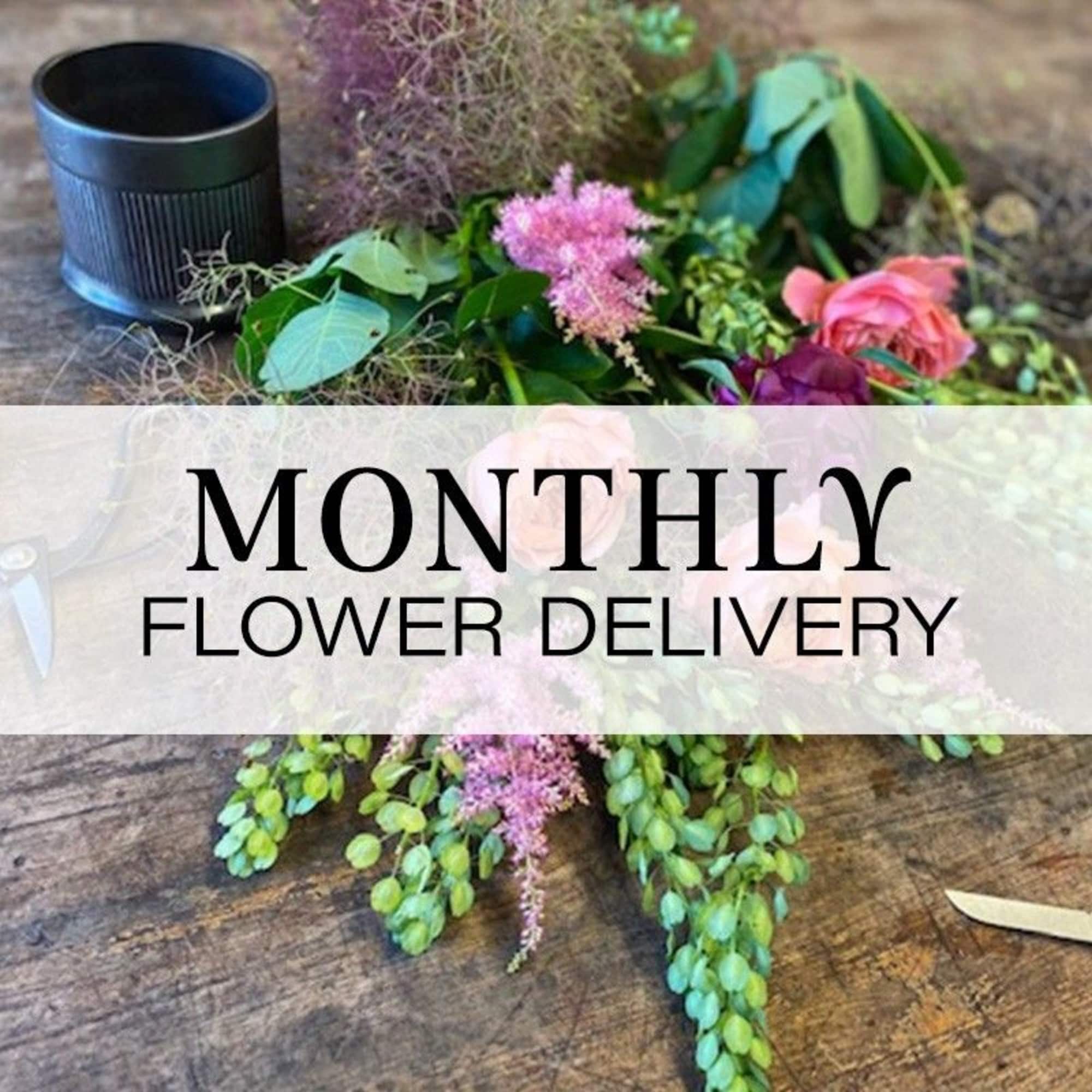 Loose flowers and greenery on a table with a black cup and monthly flower delivery text