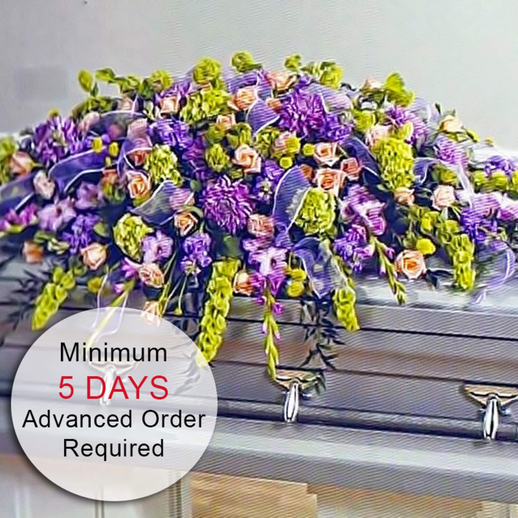 Large purple, green, and peach flower casket spray draped over a silver casket