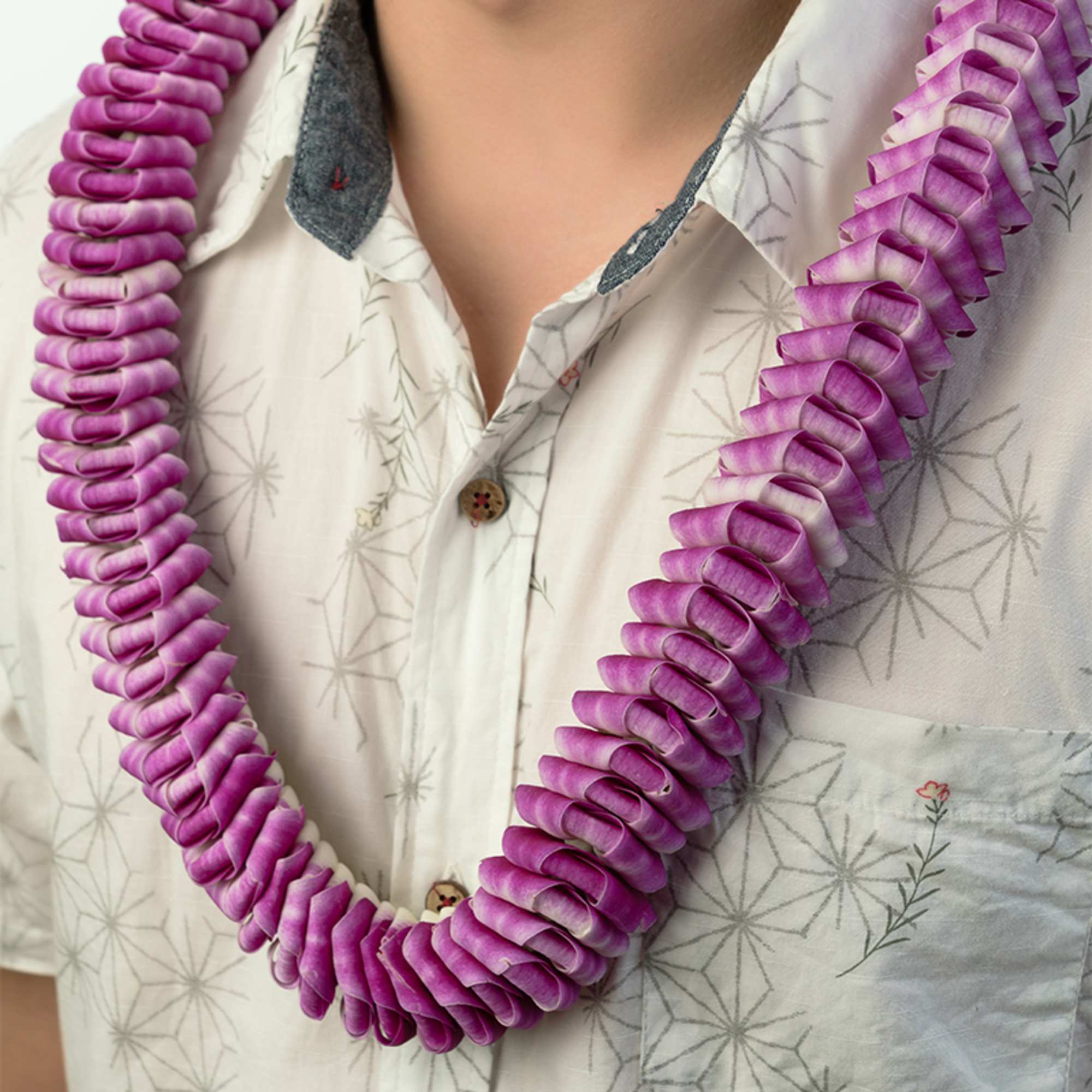 Purple orchid petal lei worn around a person’s neck over a patterned shirt