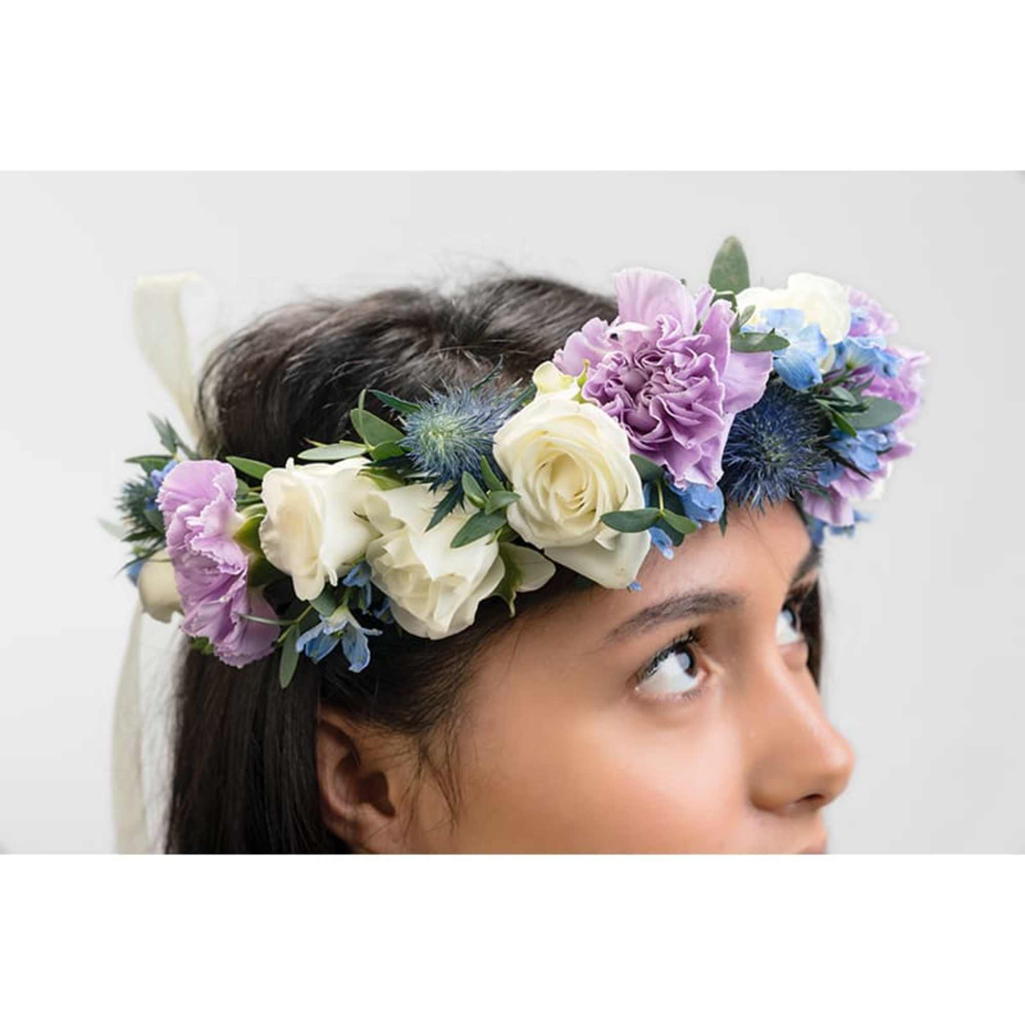 Flower crown of white roses, lavender blooms, and blue accents worn on a woman’s head.