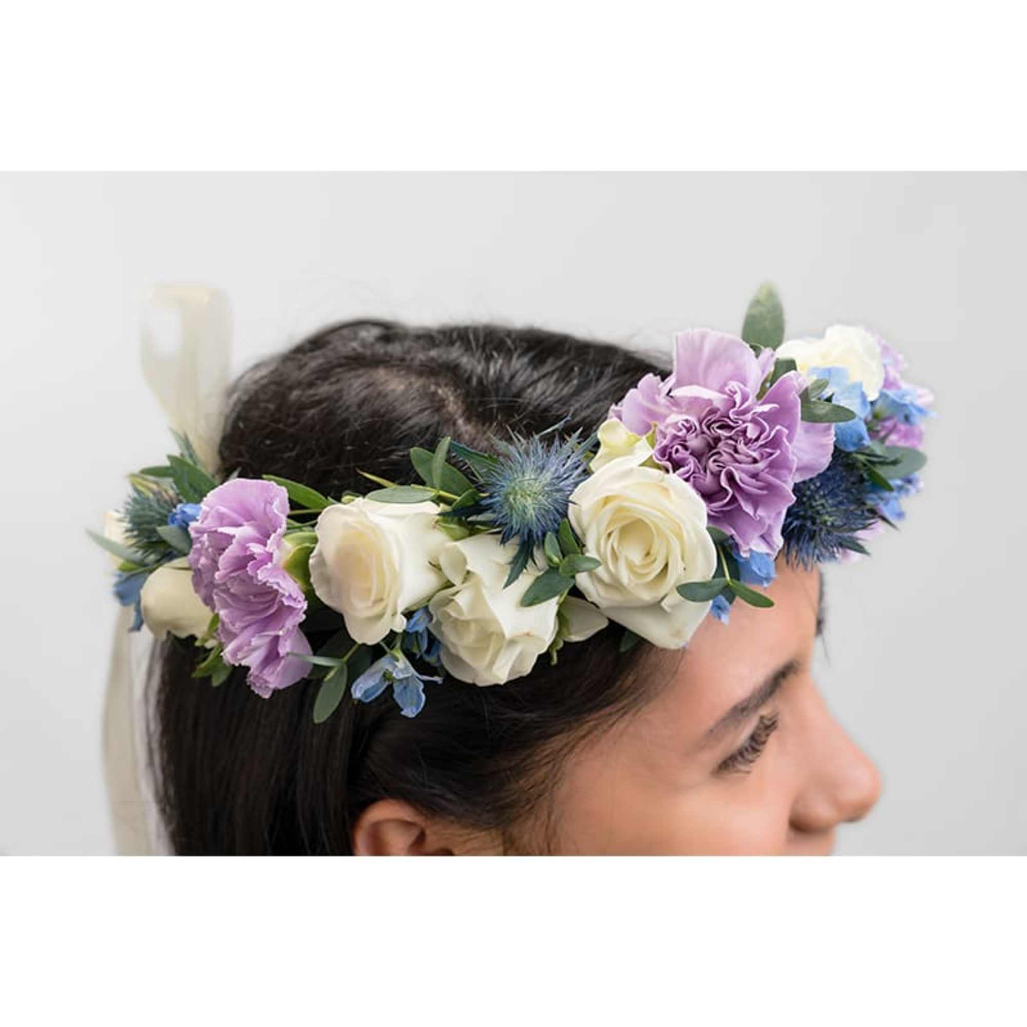Floral crown of white roses and purple flowers worn on a person’s head