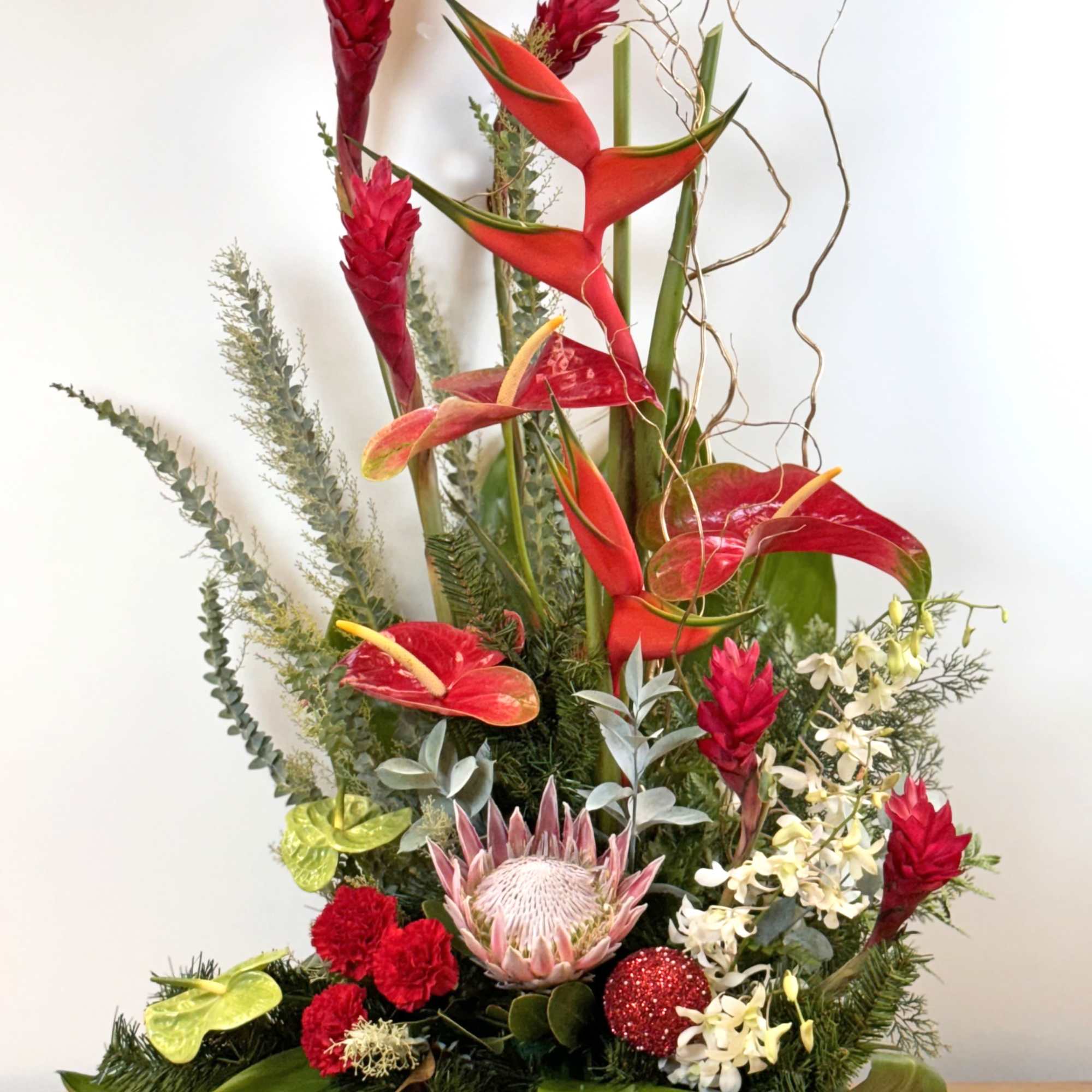 Tall tropical arrangement with red ginger, heliconia, protea, orchids and carnations in a low black container