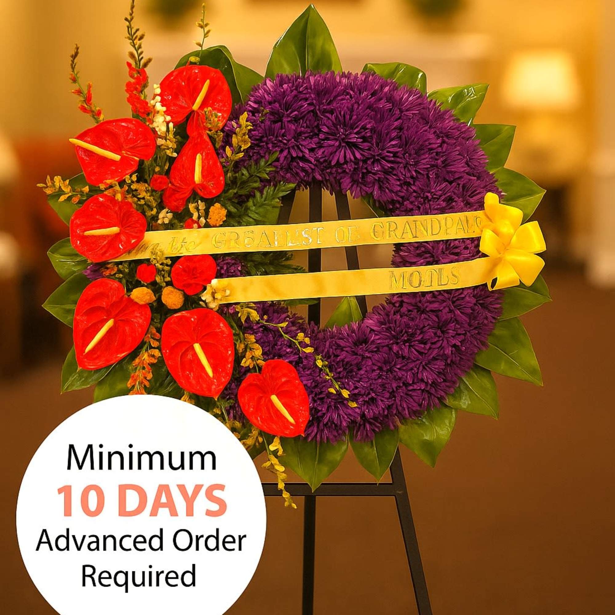 Standing purple wreath with red tropical flowers, yellow ribbon, and bow on a black easel.