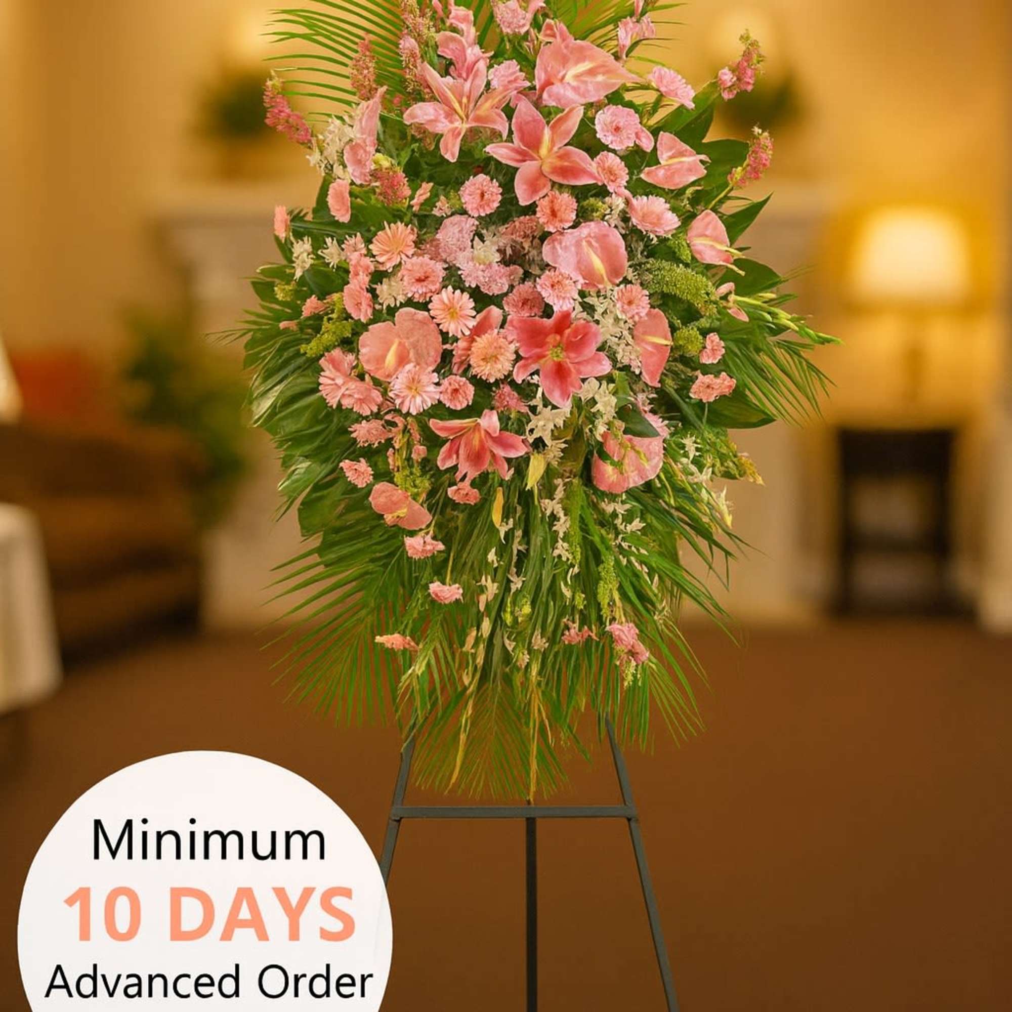 Tall pink standing spray of lilies and carnations with palm leaves on a black easel