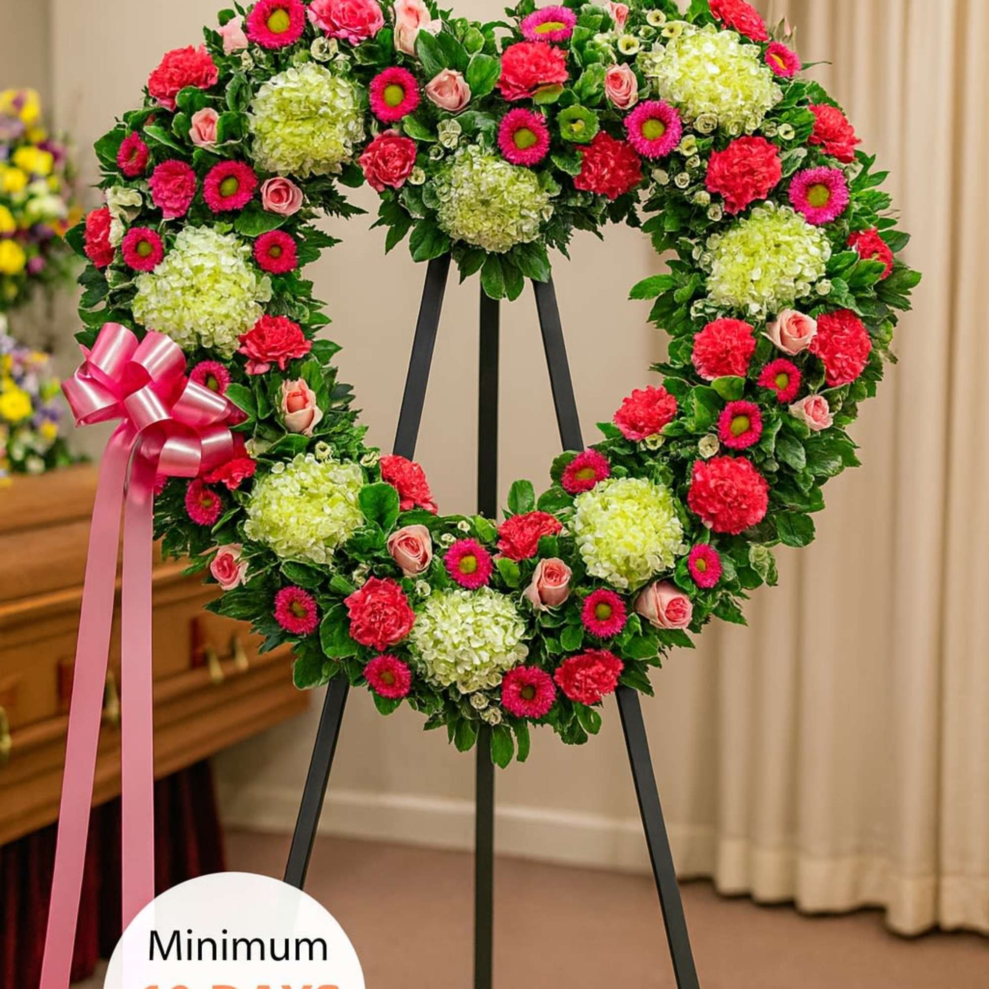 Heart-shaped standing wreath with green hydrangeas, pink roses, and bright pink flowers on a black easel.
