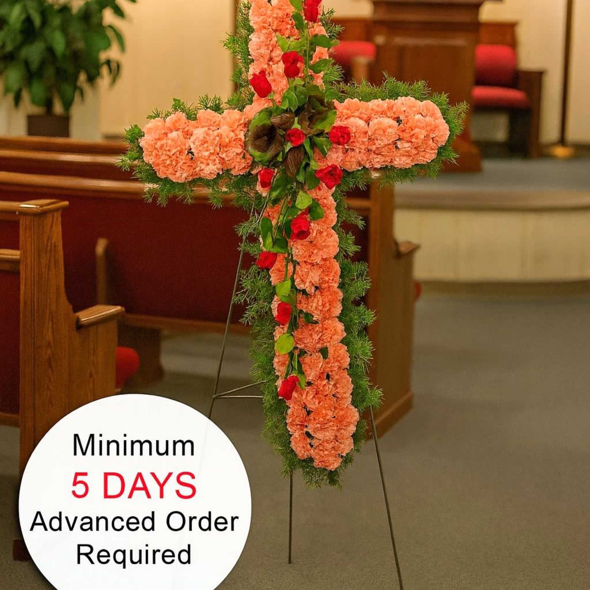 Tall peach carnation cross with red roses and greenery on an easel in a church