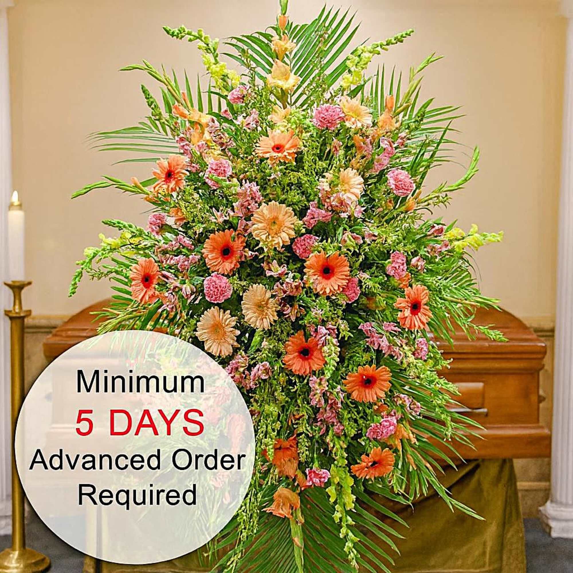 Tall funeral spray of orange gerbera daisies and mixed pink flowers with palms in front of a casket