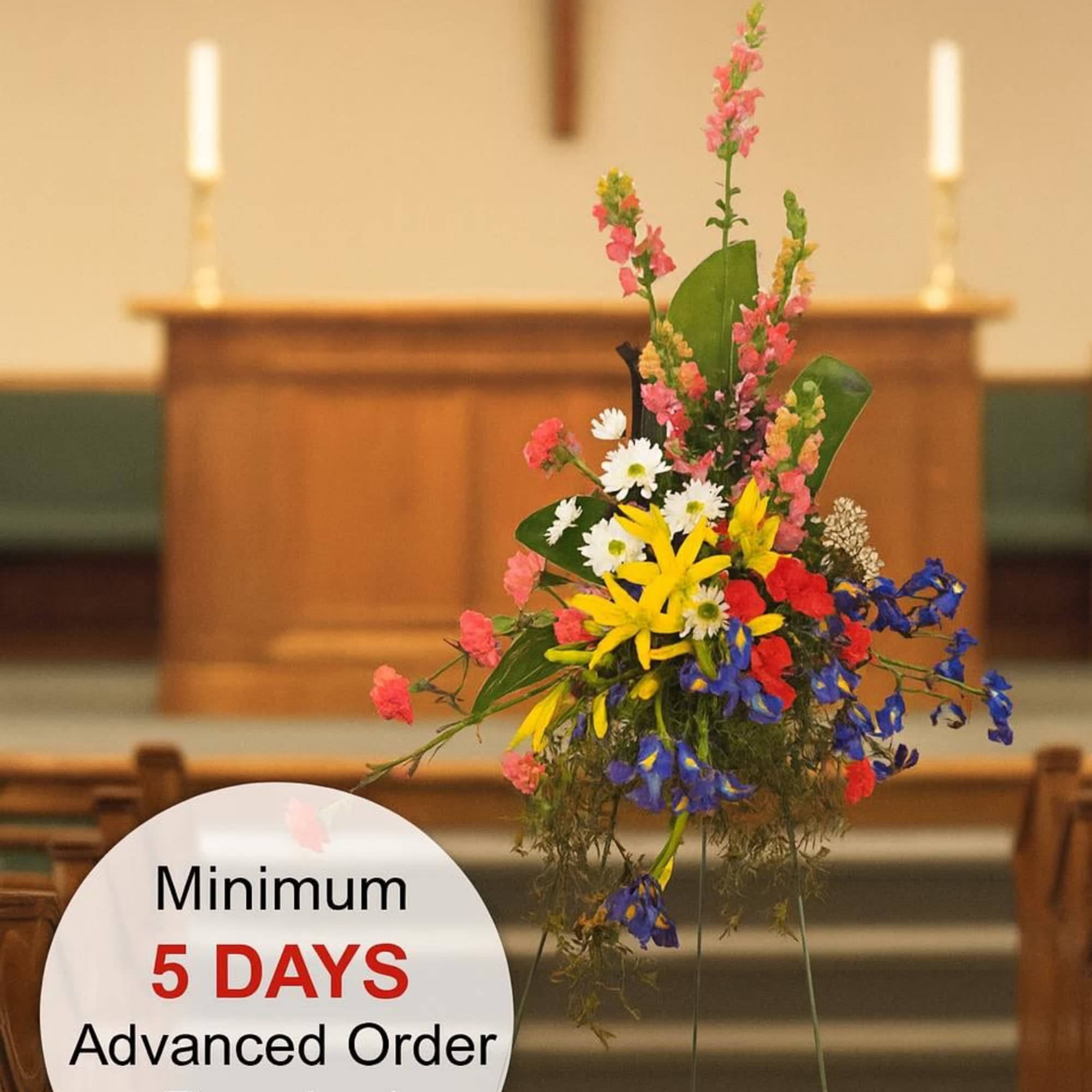 Tall multicolored standing spray with yellow lilies and mixed flowers on an easel in a church.