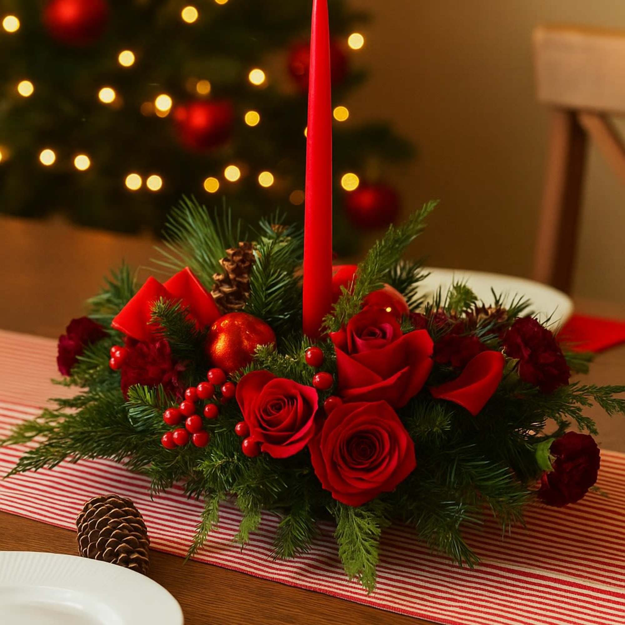 Holiday centerpiece of red roses, berries, evergreens, and a red taper candle on a table