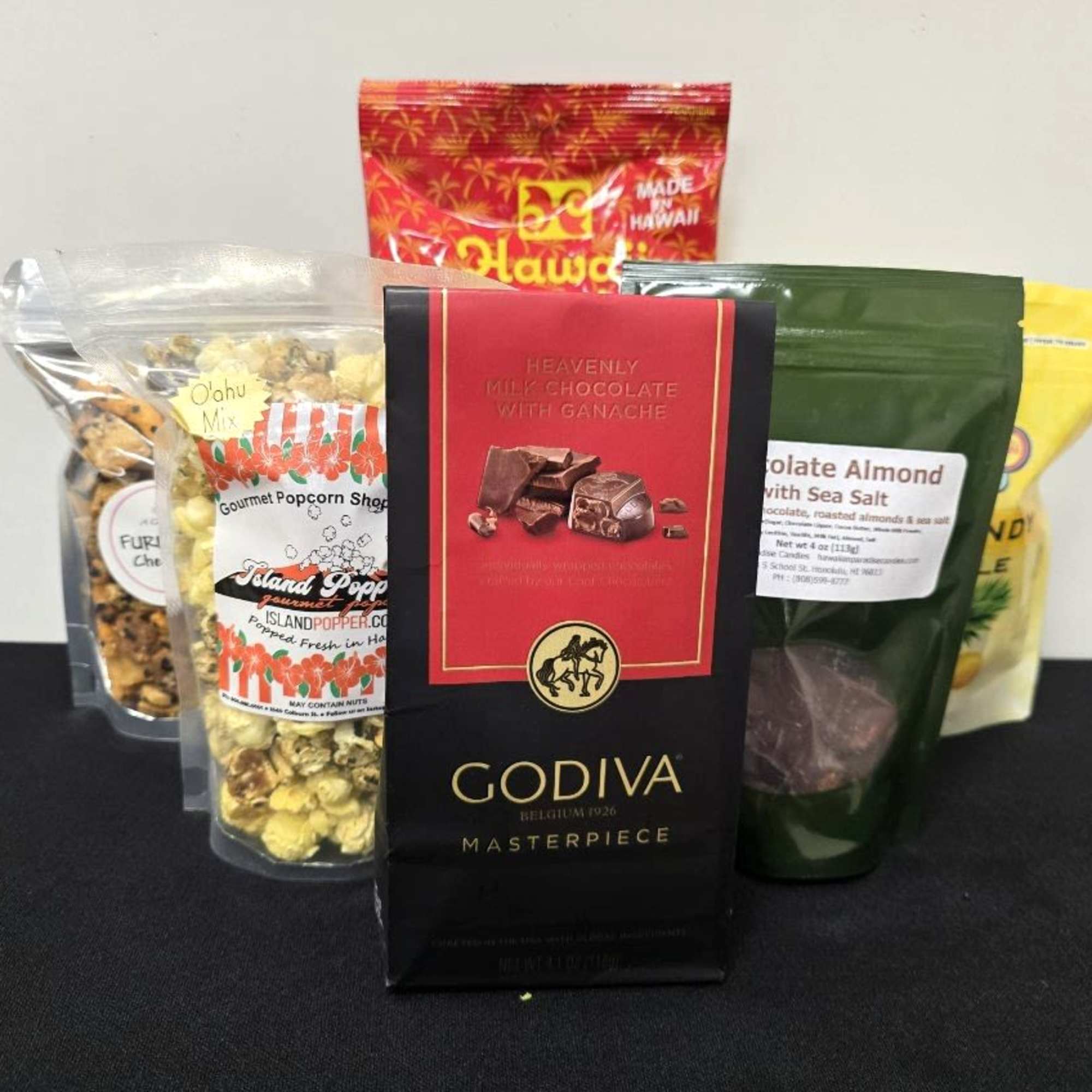 Assorted gourmet snack bags with a Godiva chocolate bar arranged on a black surface