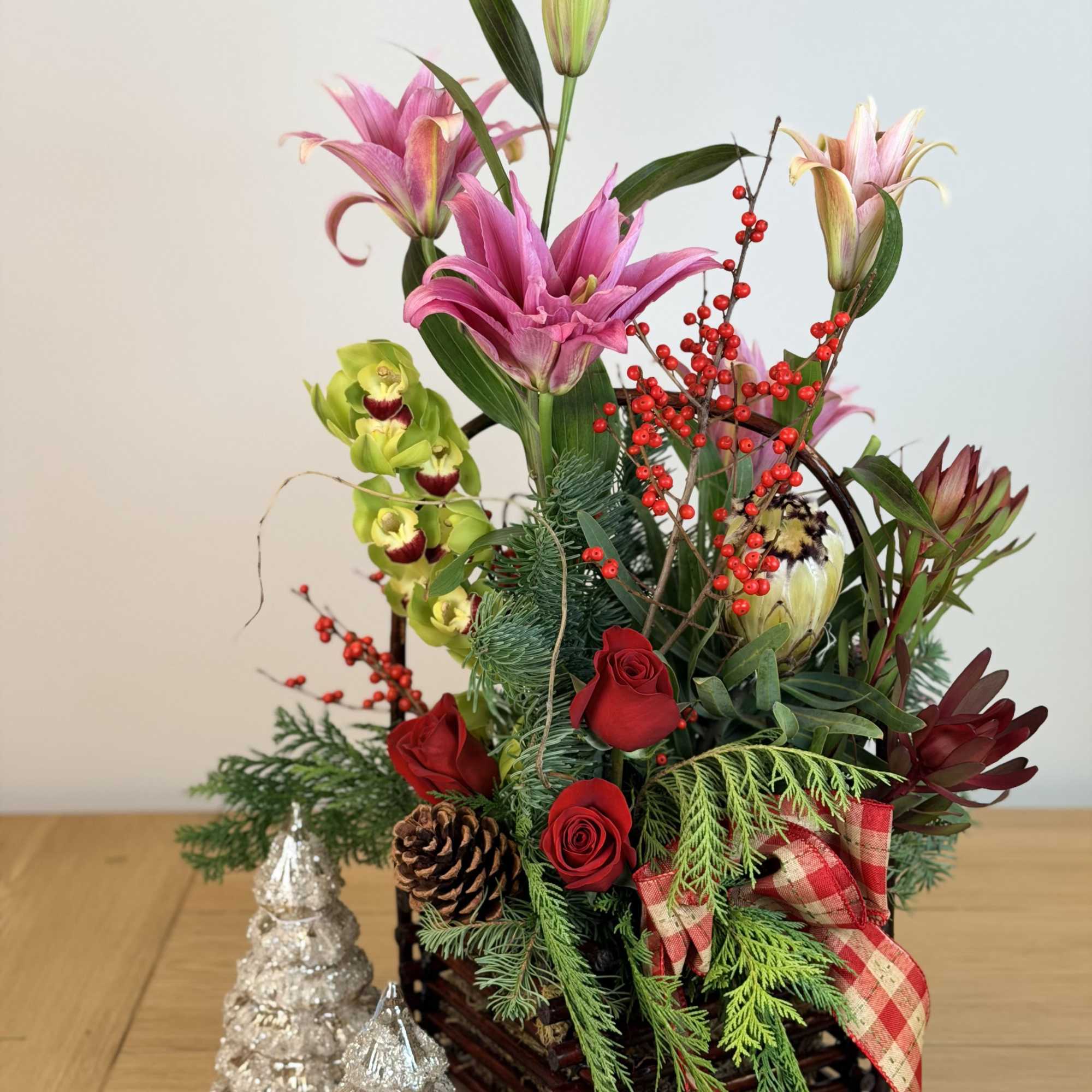 Tall holiday arrangement with pink lilies, red roses, green orchids in a twig basket with silver tree accents.
