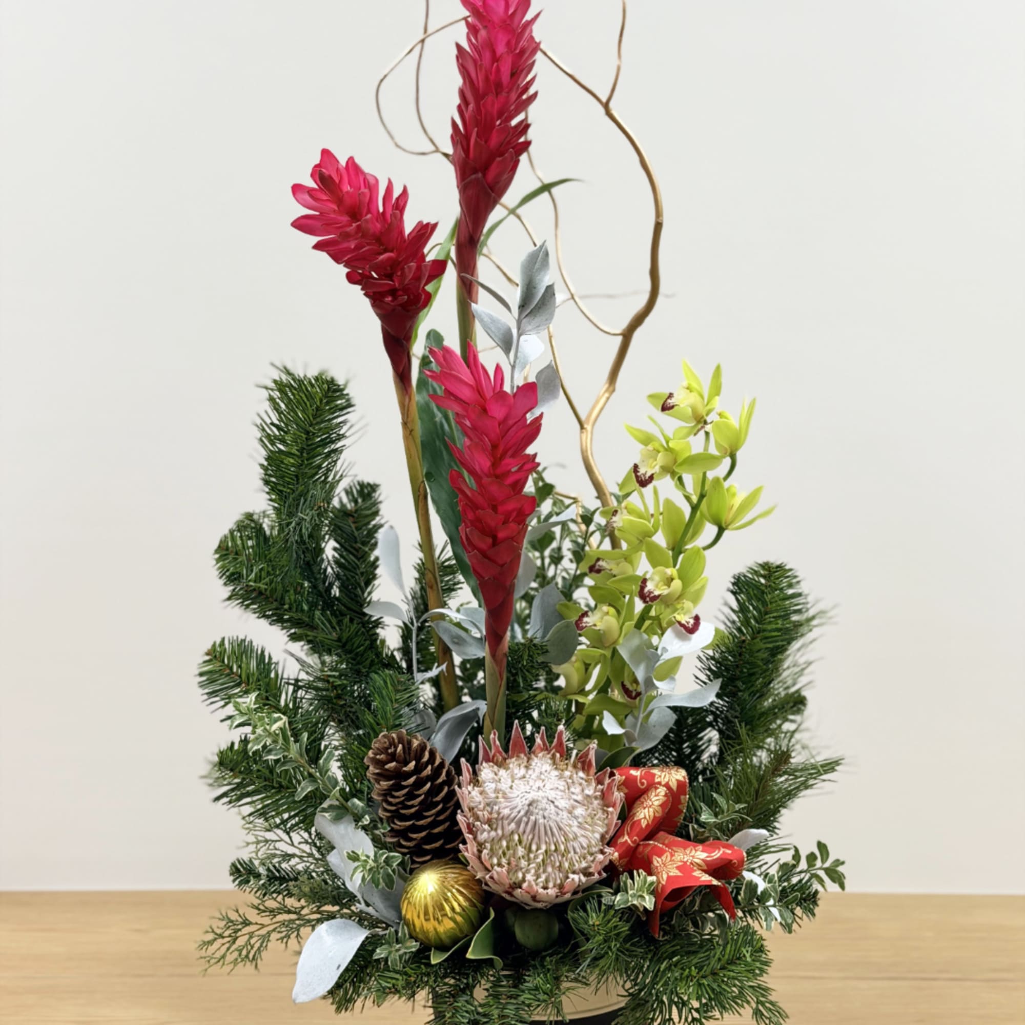 Tall floral arrangement with red and green blooms, pinecones, and a red ribbon