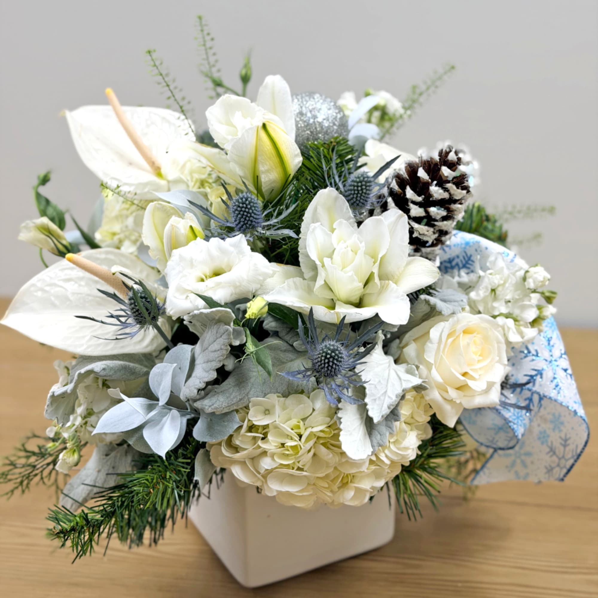 White floral arrangement in a square vase with pinecones and blue ribbon