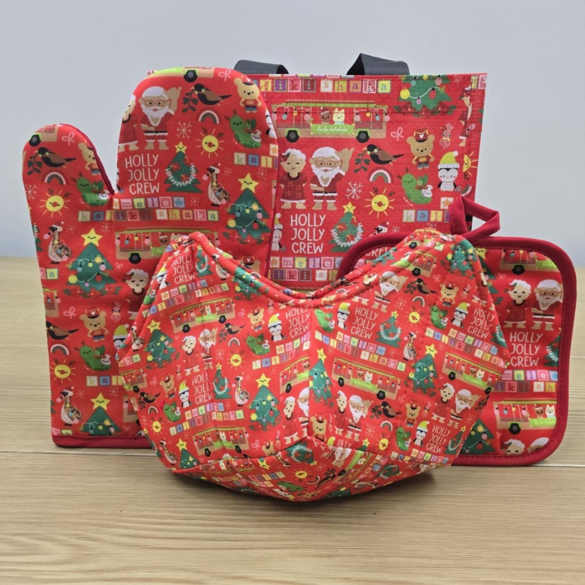 Three red Christmas oven mitts and a matching pot holder with holiday prints