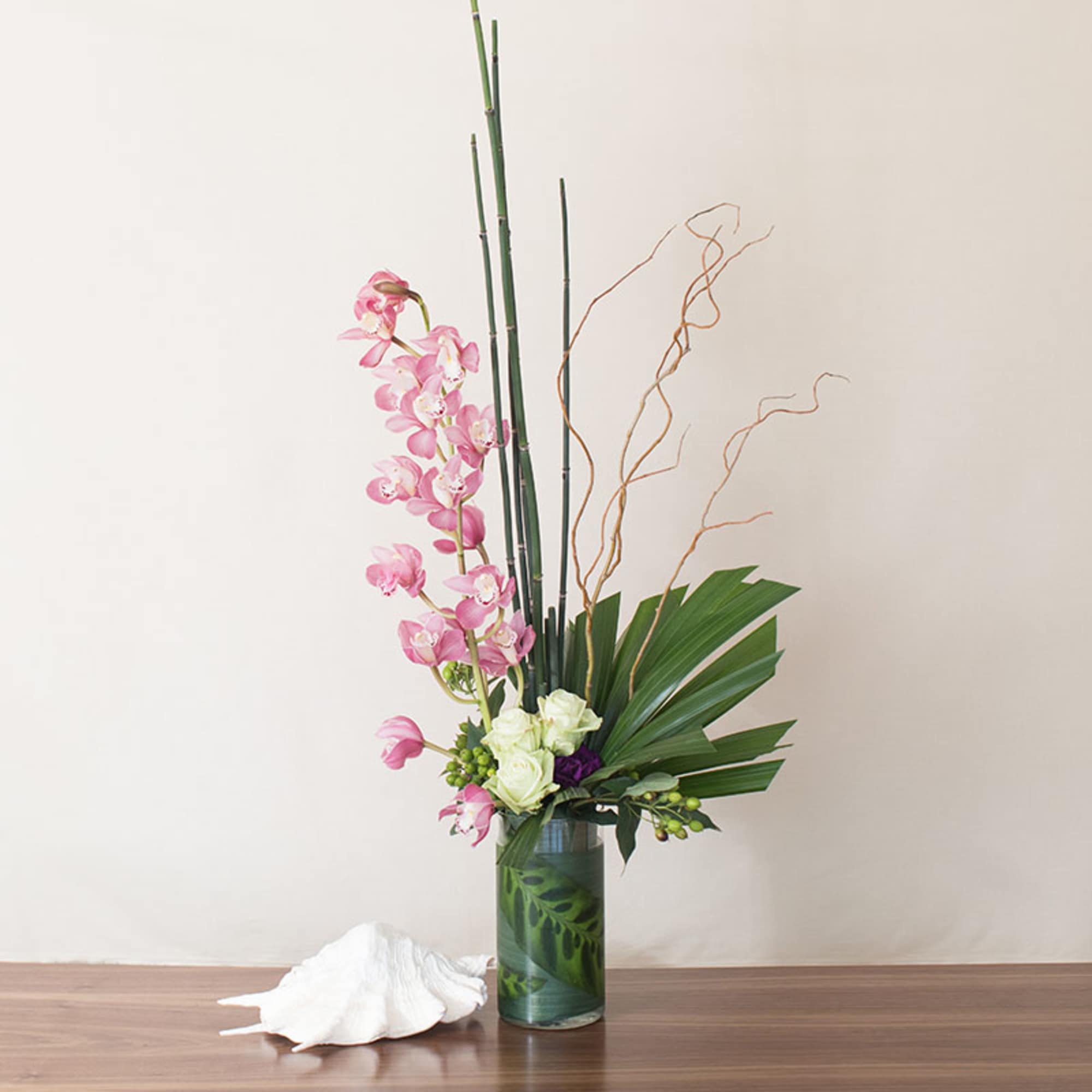 Tall modern arrangement with pink orchids and white roses in a clear cylinder vase