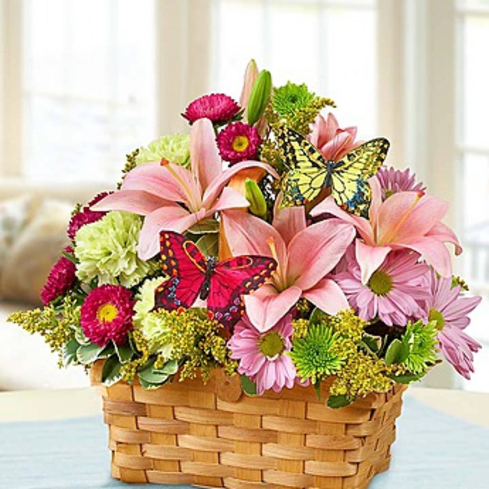 Basket arrangement of pink lilies and daisies with butterfly picks